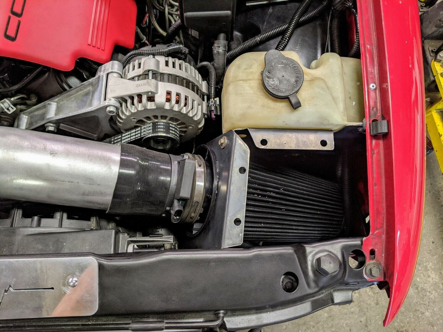 Close-up of a red 1995-2005 Chevy S10 Blazer with a custom fabricated LS Swap Cold Air Box by The Ugly Truckling, featuring a red engine cover, alternator, black cone air filter, and translucent coolant reservoir.