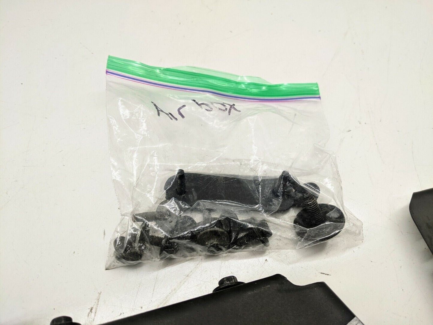 A clear Airbox-labeled bag from The Ugly Truckling contains black fasteners and screws for the 1995-2005 Chevy S10 Blazer LS Swap Cold Air Box, shown on a white surface with an LS-swapped Chevrolet S10 in view.