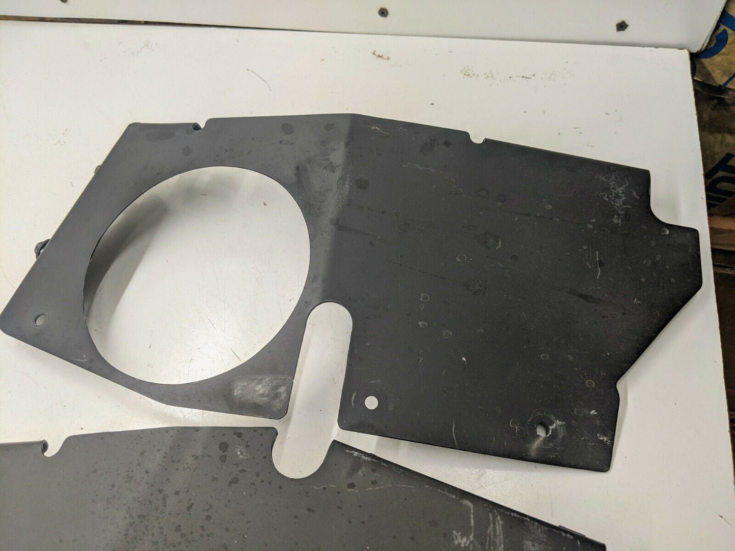 A custom fabricated flat black metal air box panel by The Ugly Truckling for 1995-2005 Chevy S10 Blazer LS swaps, featuring a large round cutout, small rectangular slot, and holes, rests on a scratched white surface.