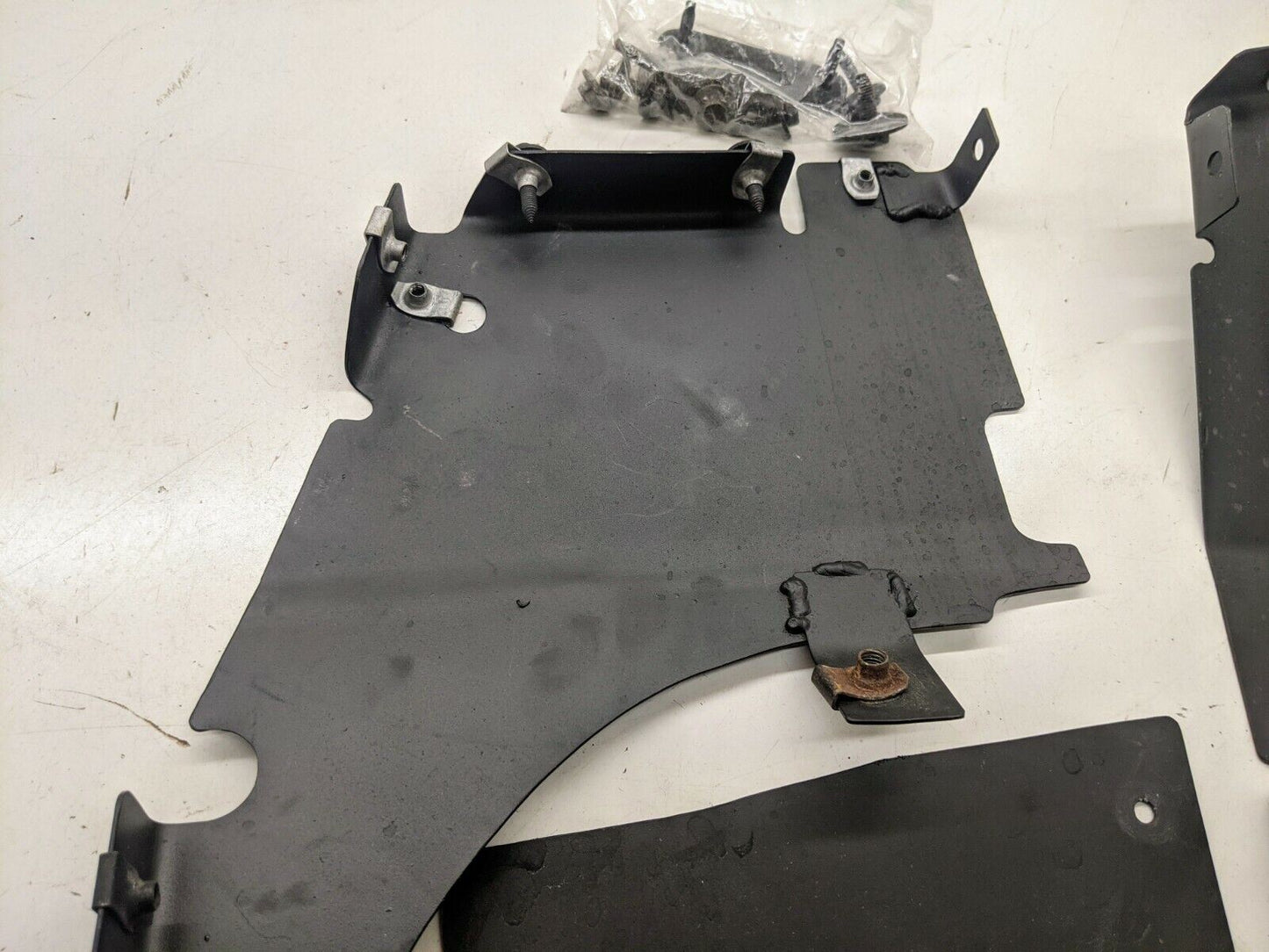 A black metal bracket from The Ugly Truckling, designed for the 1995-2005 Chevy S10 Blazer LS Swap Cold Air Box, features several mounting points and a rust spot. It rests on a white surface with included screws and fasteners nearby.