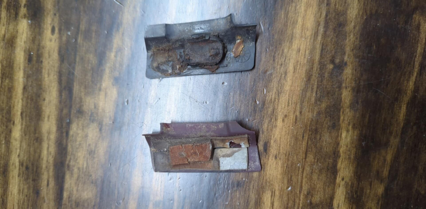 A pair of small, worn OEM General Motors rear window molding trim panel covers for 1991-1994 Chevy S10, Blazer, and GMC S15 Jimmy lie on a wooden surface, showing rust and signs of age.
