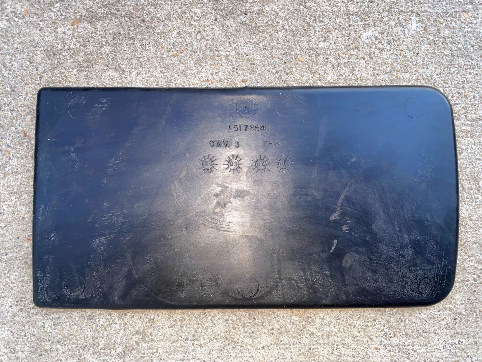 A black General Motors OEM Center Console Storage Bin Rubber Mat Liner for 2003-2006 Chevy Silverado GMC Sierra features faint circular marks and embossed sun symbols, “CAV 3,” and “TES,” shown on a rough concrete surface.