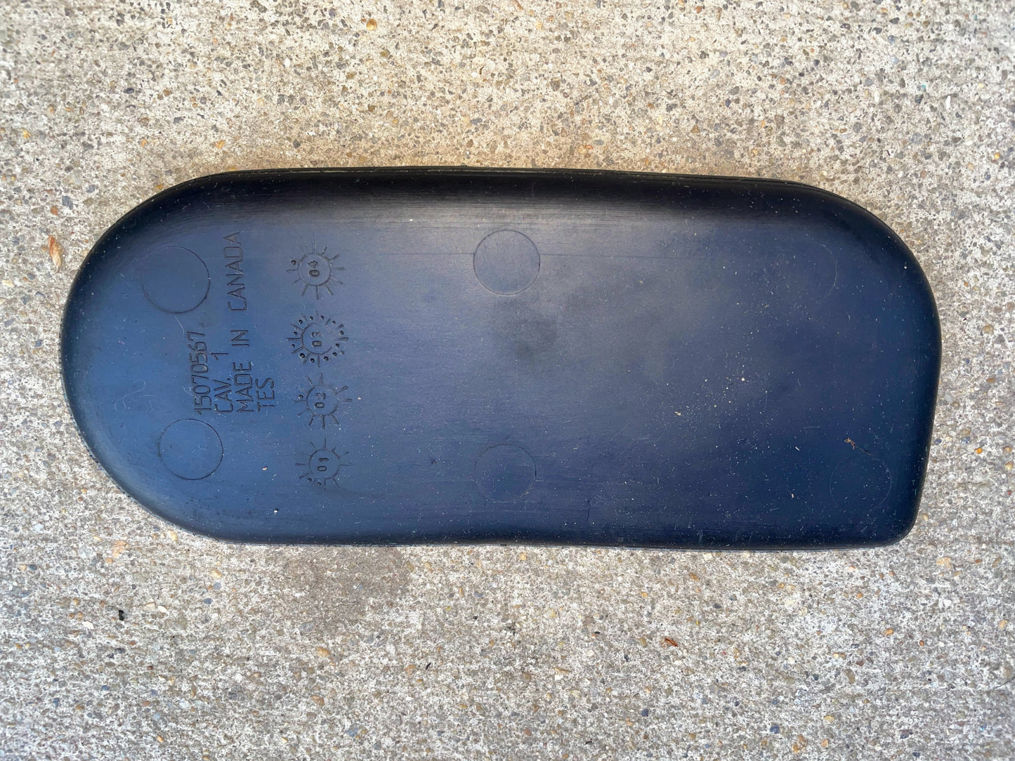 A black, curved rubber OEM Center Console Cup Holder Accessory Bin Mat by General Motors, for 2003-2006 Chevy Silverado/GMC Sierra, with embossed MADE IN CANADA and part number, rests on rough gray concrete.