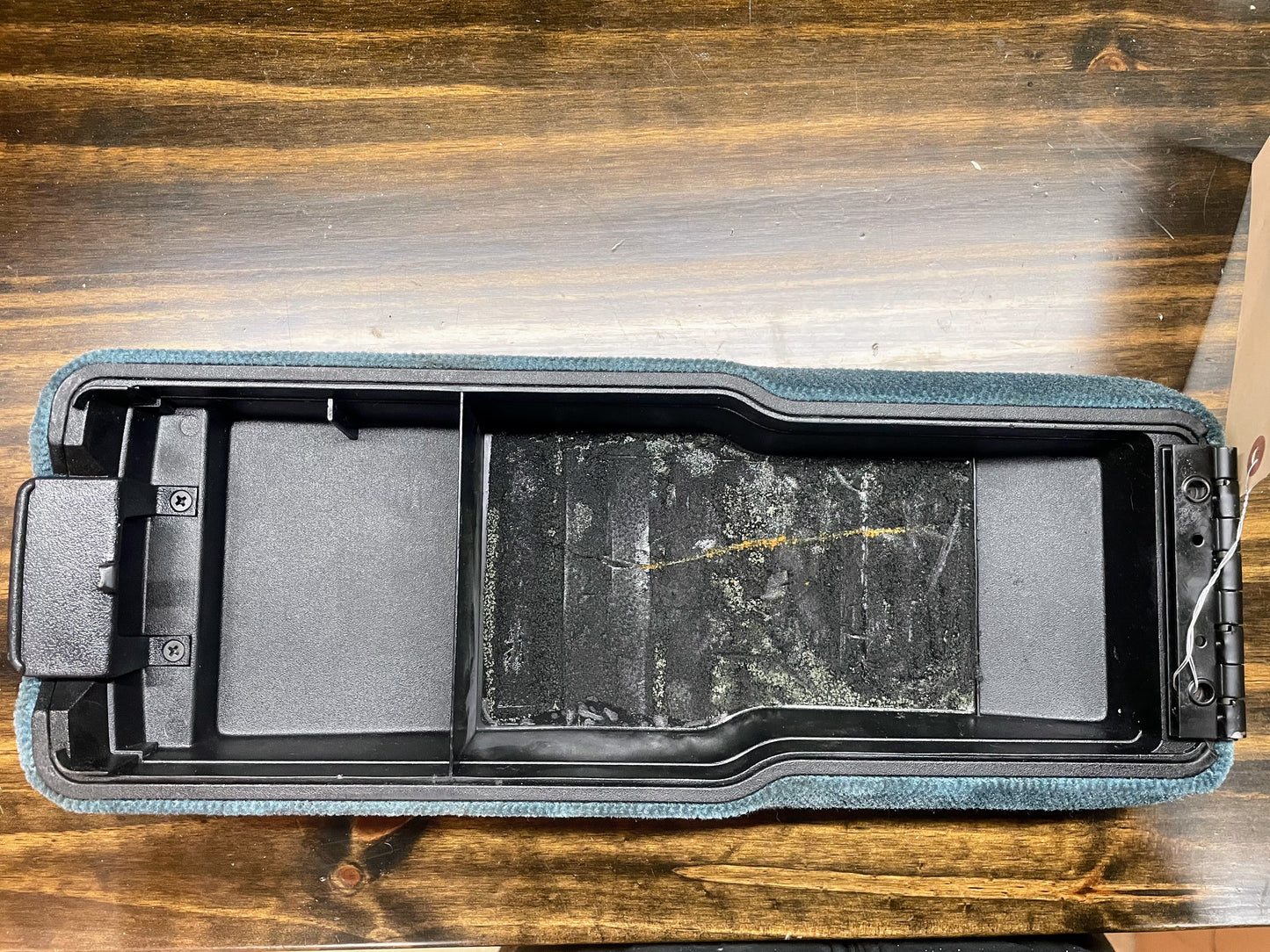 A General Motors OEM 16.5 Center Armrest 60/40 Bench Console Lid in Blue for 1994-1997 Chevy S10 GMC Sonoma sits open on a wooden surface, revealing two compartments and interior wear marks.