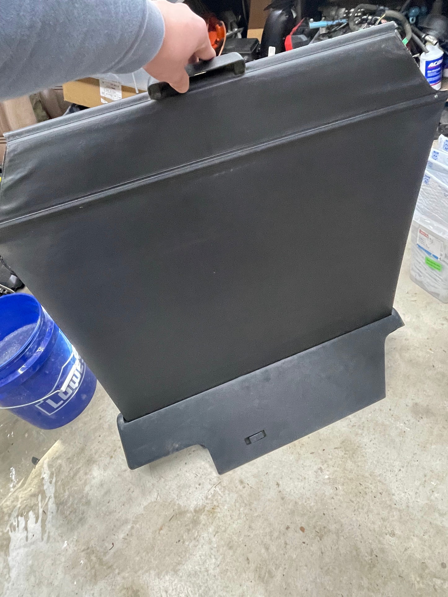 A person holds a General Motors OEM Retractable Rear Cargo Shade Jack Cover in Graphite for 1995-2005 Chevy Blazer/GMC Jimmy, standing on a concrete floor in a cluttered garage or workshop.