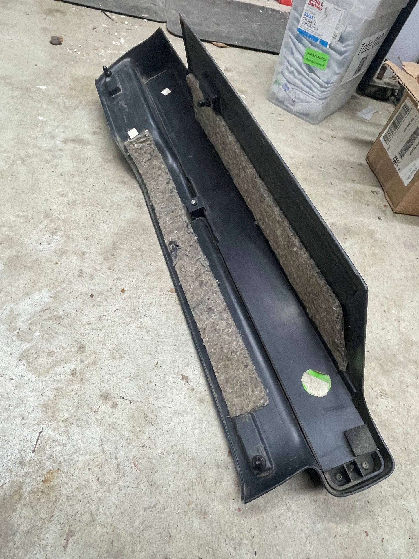 An OEM Retractable Rear Cargo Shade Jack Cover in Graphite for 1995-2005 Chevy Blazer GMC Jimmy by General Motors rests on a concrete floor, with cardboard boxes and a plastic storage bin seen in the background.