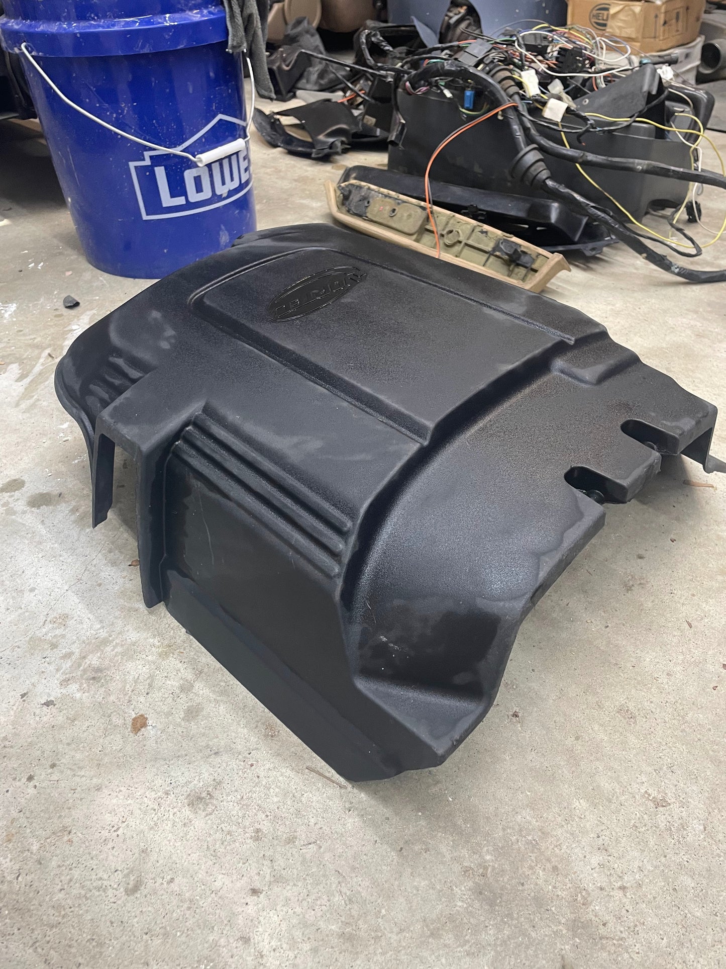 A General Motors OEM Vortec Engine Intake Cover for 2007-2019 GM Trucks and LS swaps sits on a concrete garage floor, surrounded by car parts, wiring, and a blue Lowes bucket.