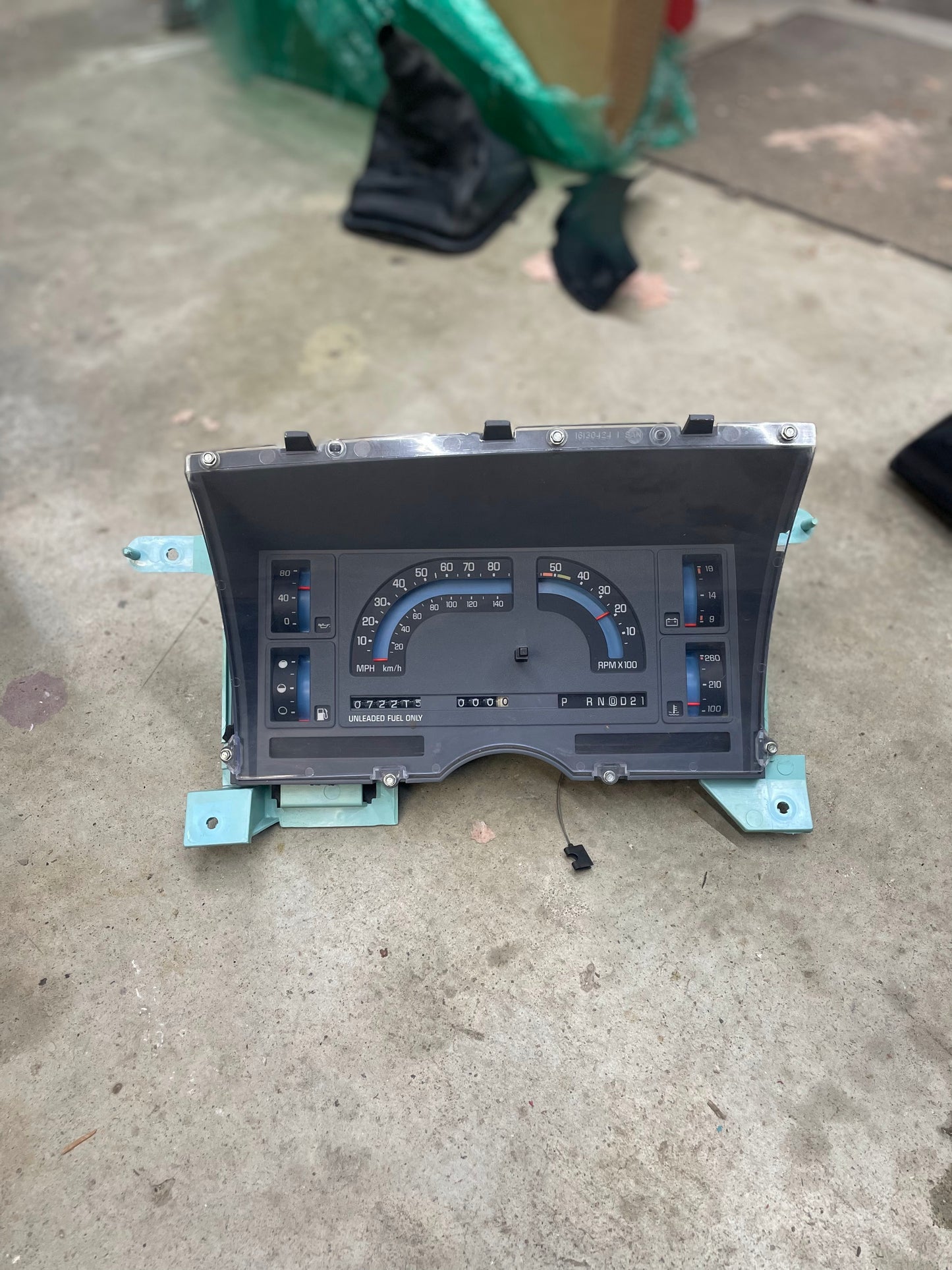 A LOW Mile 72K OEM Instrument Cluster by General Motors for 1986-1989 Chevy S10 Blazer, featuring mechanical speedometer, tachometer, and PRNDL, sits on a concrete floor in a garage or workshop.