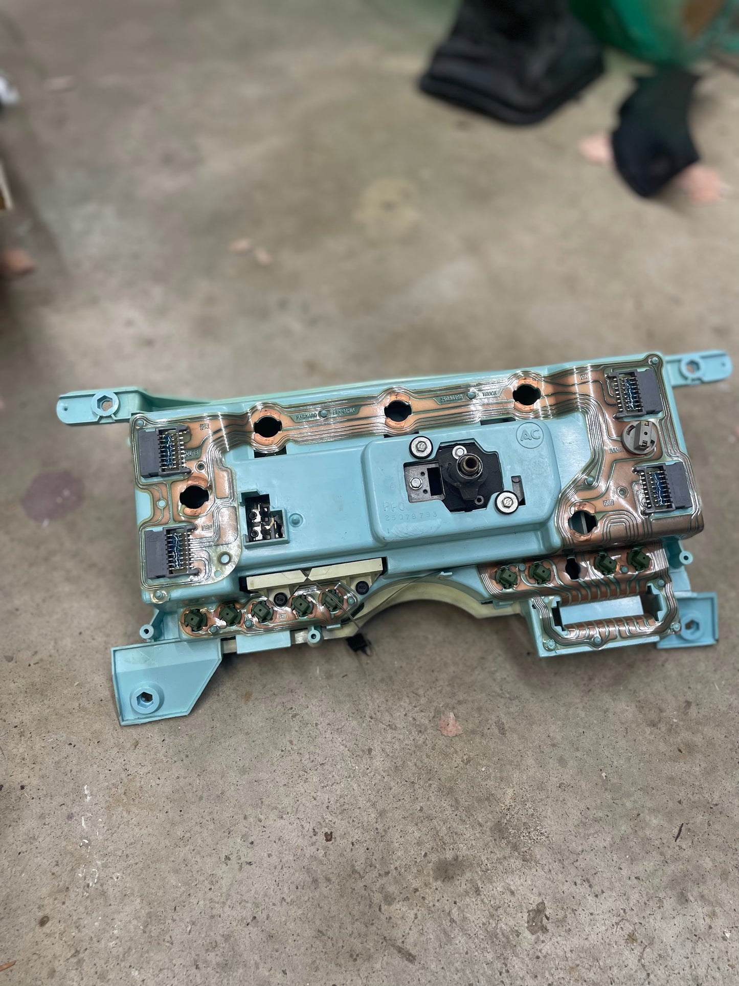 A close-up of a LOW Mile 72K OEM General Motors instrument cluster with mechanical speedo, tachometer & PRNDL for 1986-1989 Chevy S10 Blazer, showing exposed circuitry and connectors on a concrete floor.