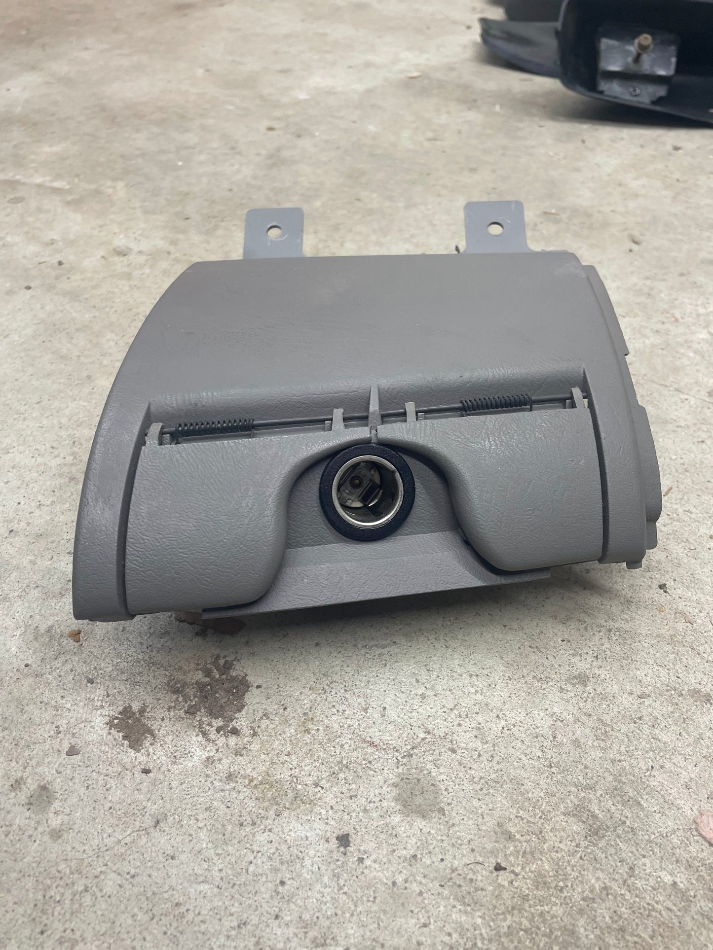 A General Motors OEM 3 Port 12V Aux Panel Ash Tray Delete in light gray from a 1998-2000 GMC Envoy sits on a concrete floor, ideal for replacing the original ashtray.