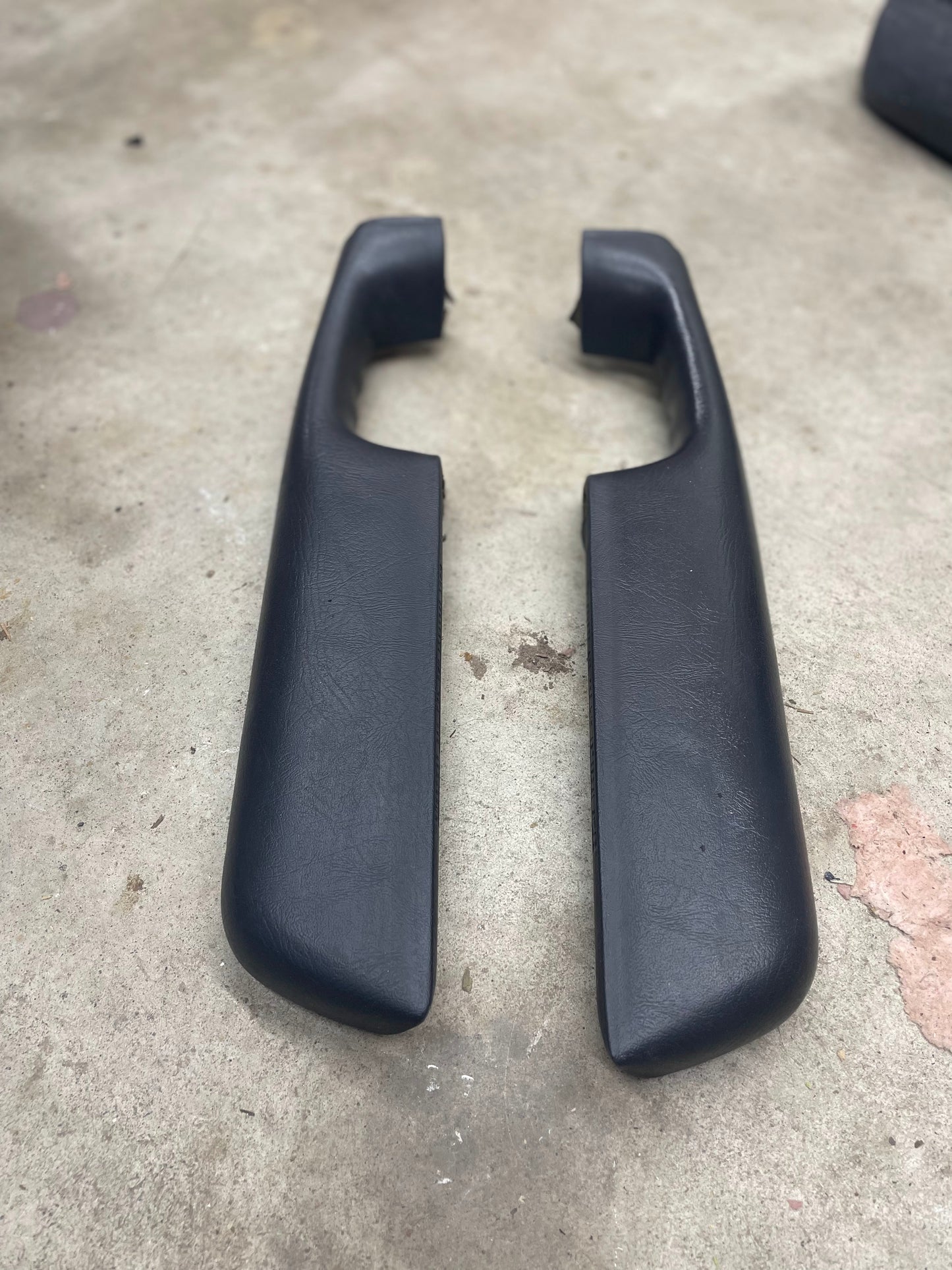 Two dark gray OEM front armrests by General Motors, made for 1998–2005 Chevy S10, Blazer, and more, are placed parallel on a concrete surface.