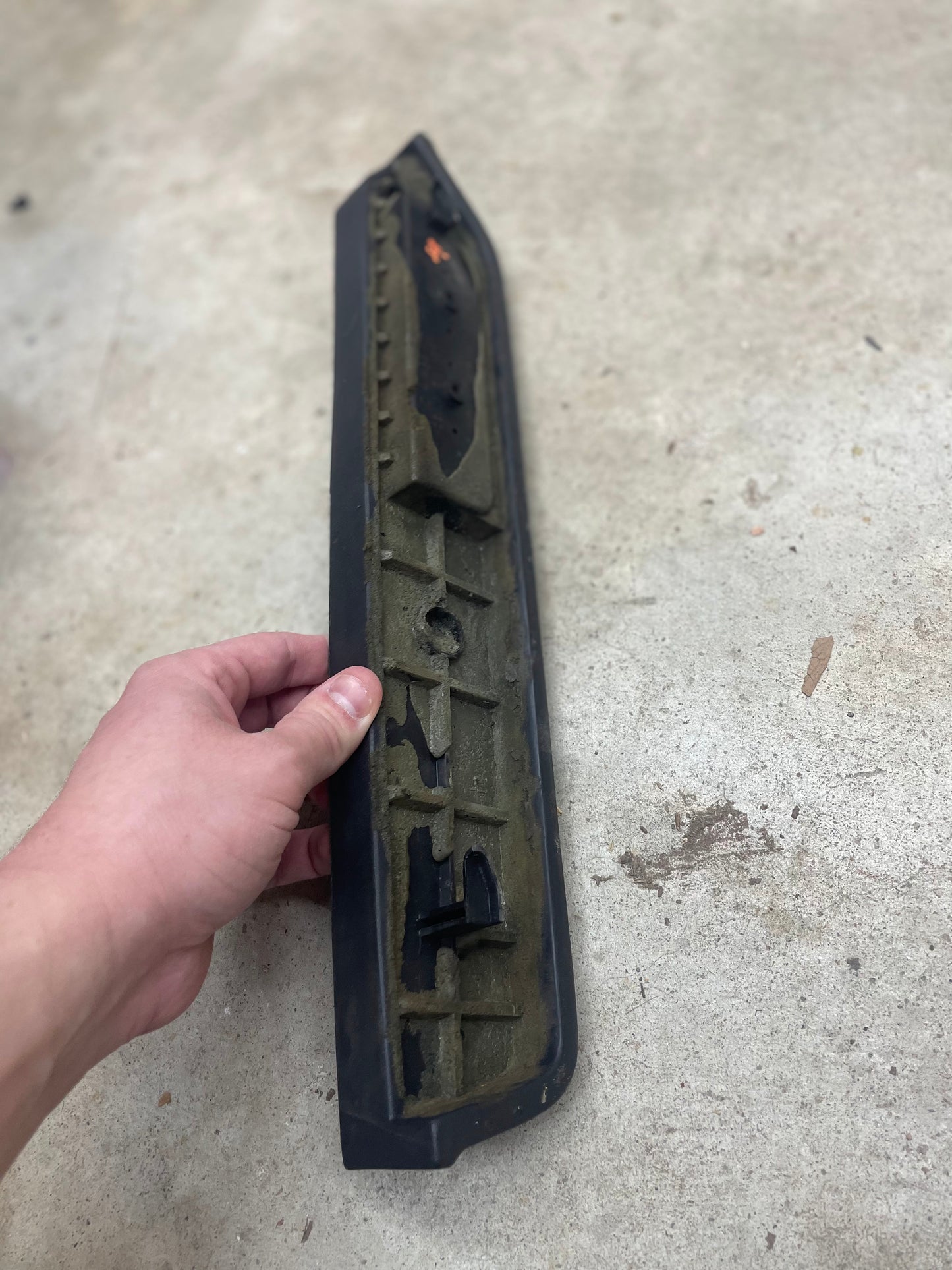 A hand holds a black OEM passenger door panel armrest handle by General Motors for 1986-1993 Chevy S10, Blazer, GMC Jimmy and more, against a concrete floor background.