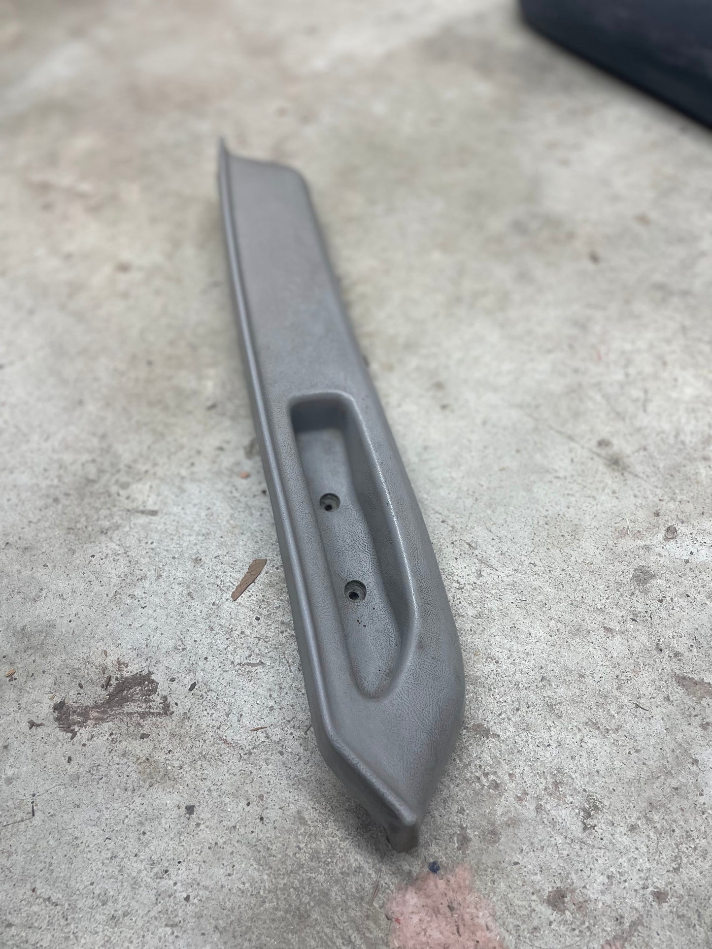 Light gray OEM passenger door armrest handle by General Motors for 1986–1993 Chevy S10 Blazer, GMC Jimmy, and more. Features a recessed section and two screw holes; minor scuffs and wear present.