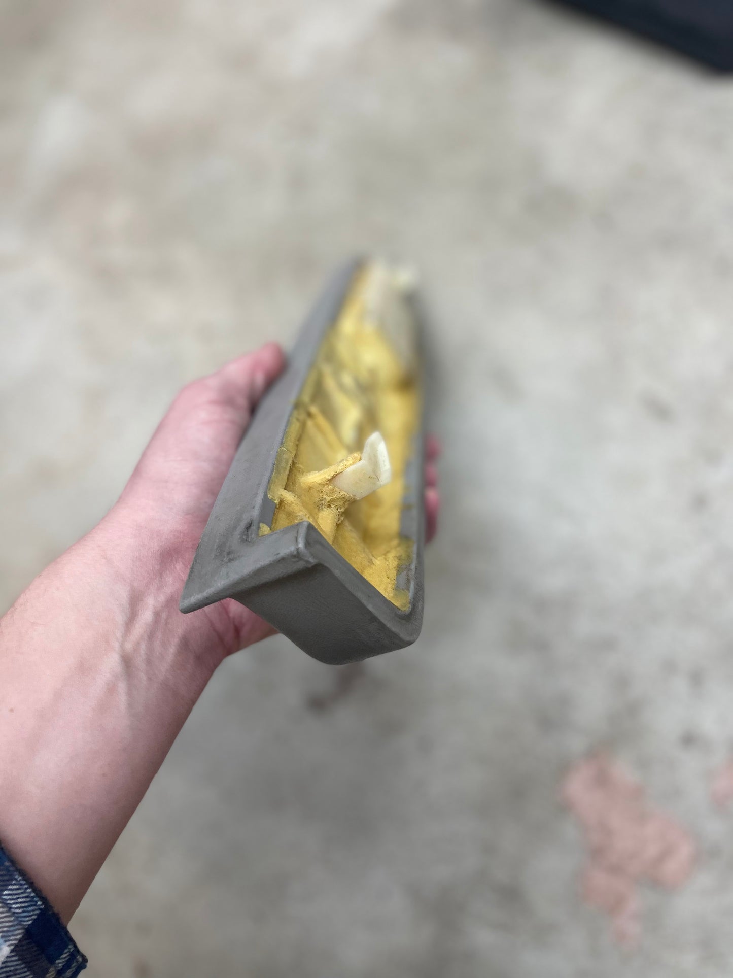A hand holds a General Motors OEM Passenger Door Panel Armrest Handle in light gray for 1986-1993 Chevy S10 Blazer and GMC Jimmy, shown against a blurred, light-colored background.