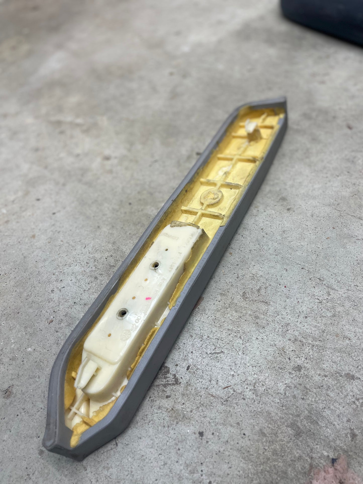A long General Motors OEM passenger door panel armrest handle in light gray for 1986-1993 Chevy S10, Blazer, GMC Jimmy, and more rests on a concrete floor with exposed yellow foam and visible white internal support.