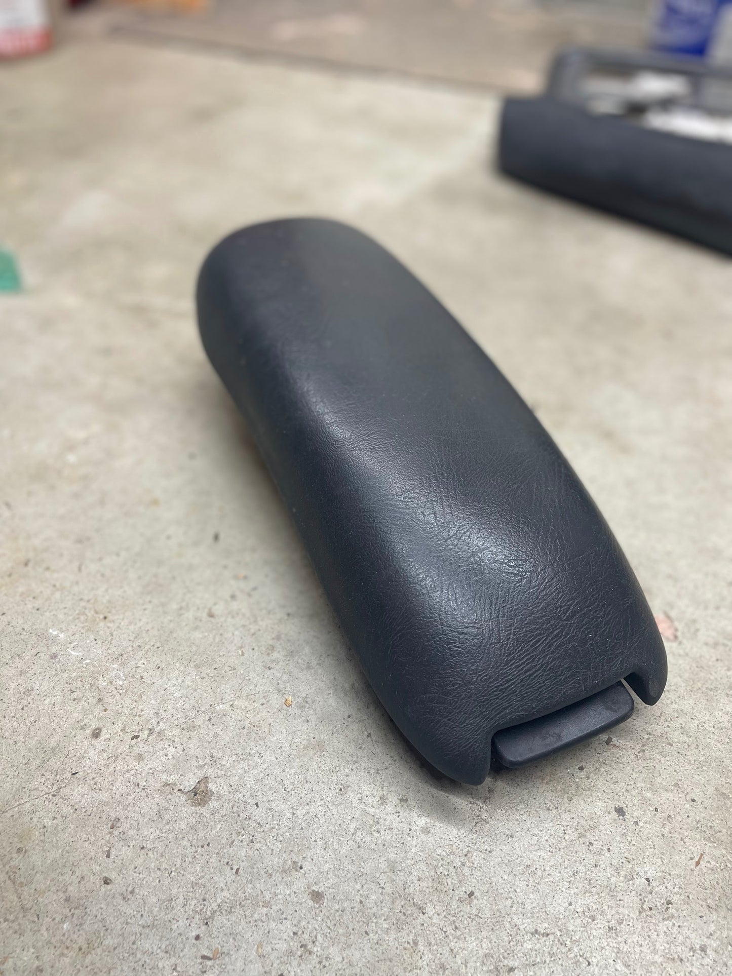 A General Motors OEM Center Console Lid Armrest in Dark Gray for 1998-2005 Chevy S10 and Blazer rests on a concrete floor—an ideal replacement part for vehicles with GM Graphite interior.