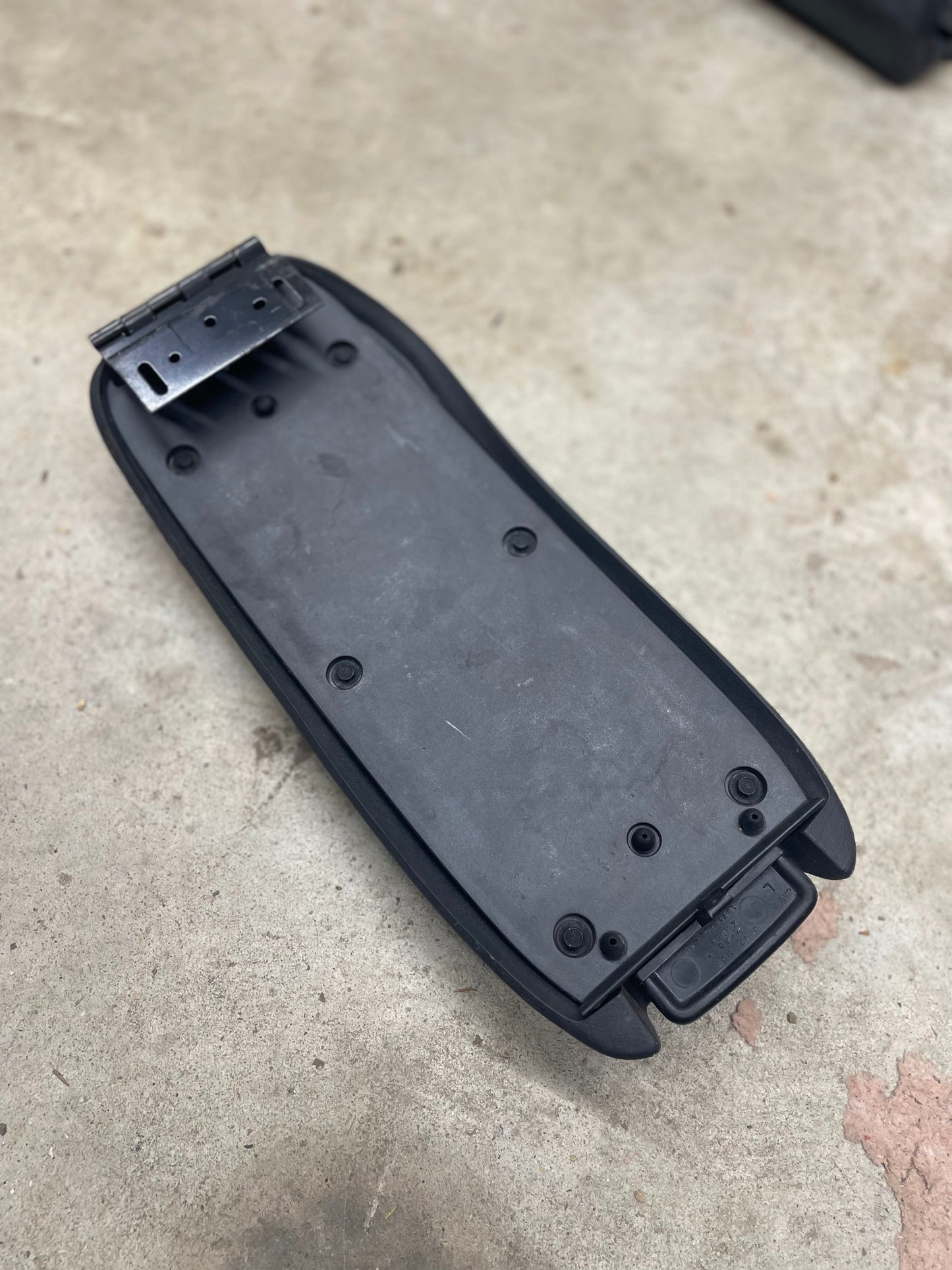 A General Motors OEM center console lid armrest in dark gray for 1998-2005 Chevy S10, Blazer, and more sits on a rough, light-colored concrete surface.