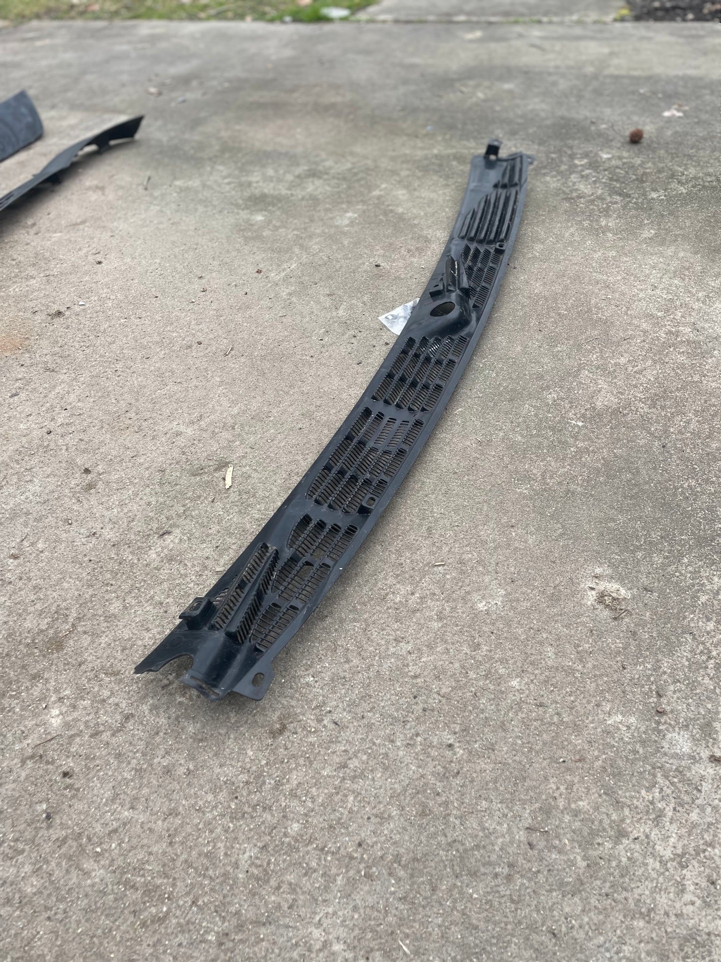 A General Motors OEM Wiper Cowl Cover Center Trim with texture for 1994-2005 Chevrolet S10, Blazer, and more is on a concrete surface outdoors, with grass visible in the background.