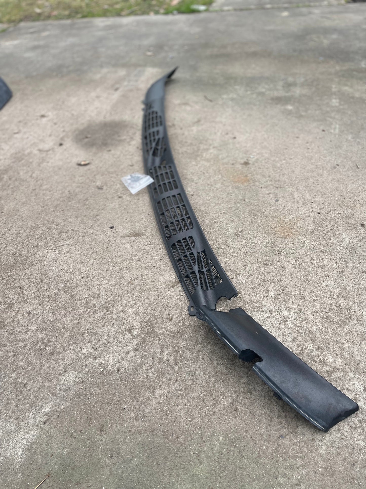 A General Motors OEM Wiper Cowl Cover Set with texture for 1994-2005 Chevrolet S10, Blazer, and more is shown outdoors on concrete with vent openings visible; a small plastic bag and grass are nearby.