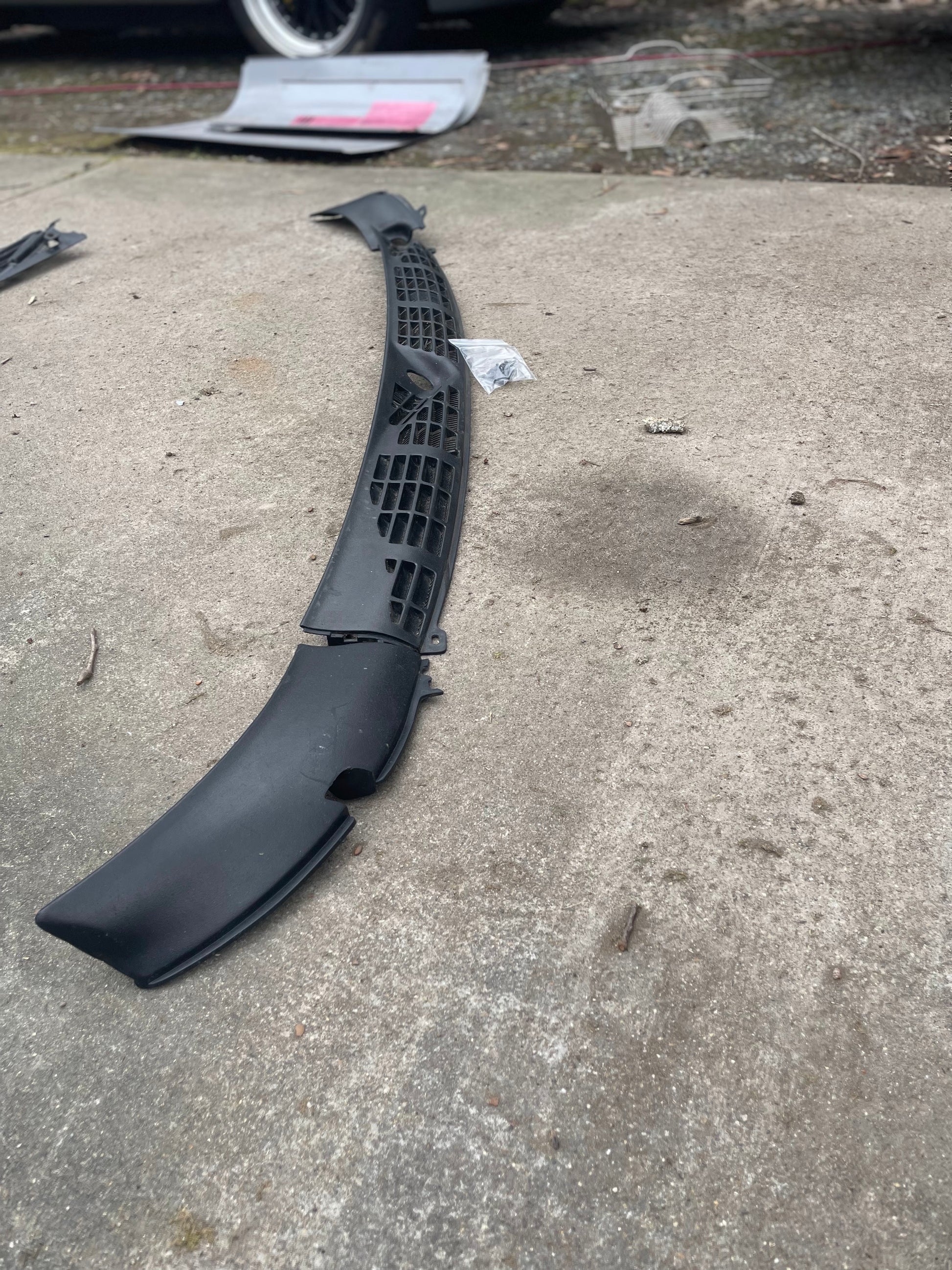 A black General Motors OEM Wiper Cowl Cover Set with texture for 1994-2005 Chevrolet S10, Blazer, and more is lying on concrete outdoors, with a Chevrolet Blazer tire and some tools visible in the background.