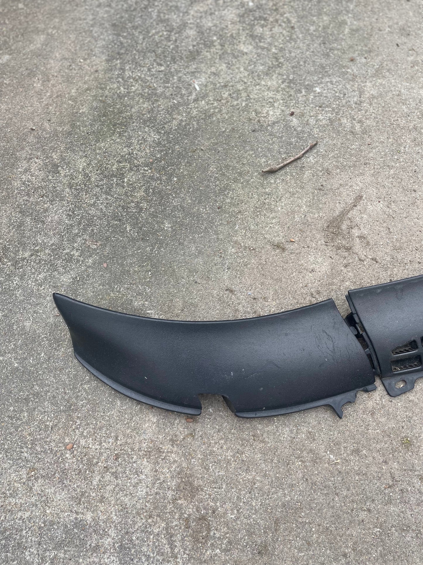 A black General Motors OEM Wiper Cowl Cover Set with texture for 1994-2005 Chevrolet S10, Blazer, and more is on a rough gray concrete surface near a twig, with one end appearing broken.