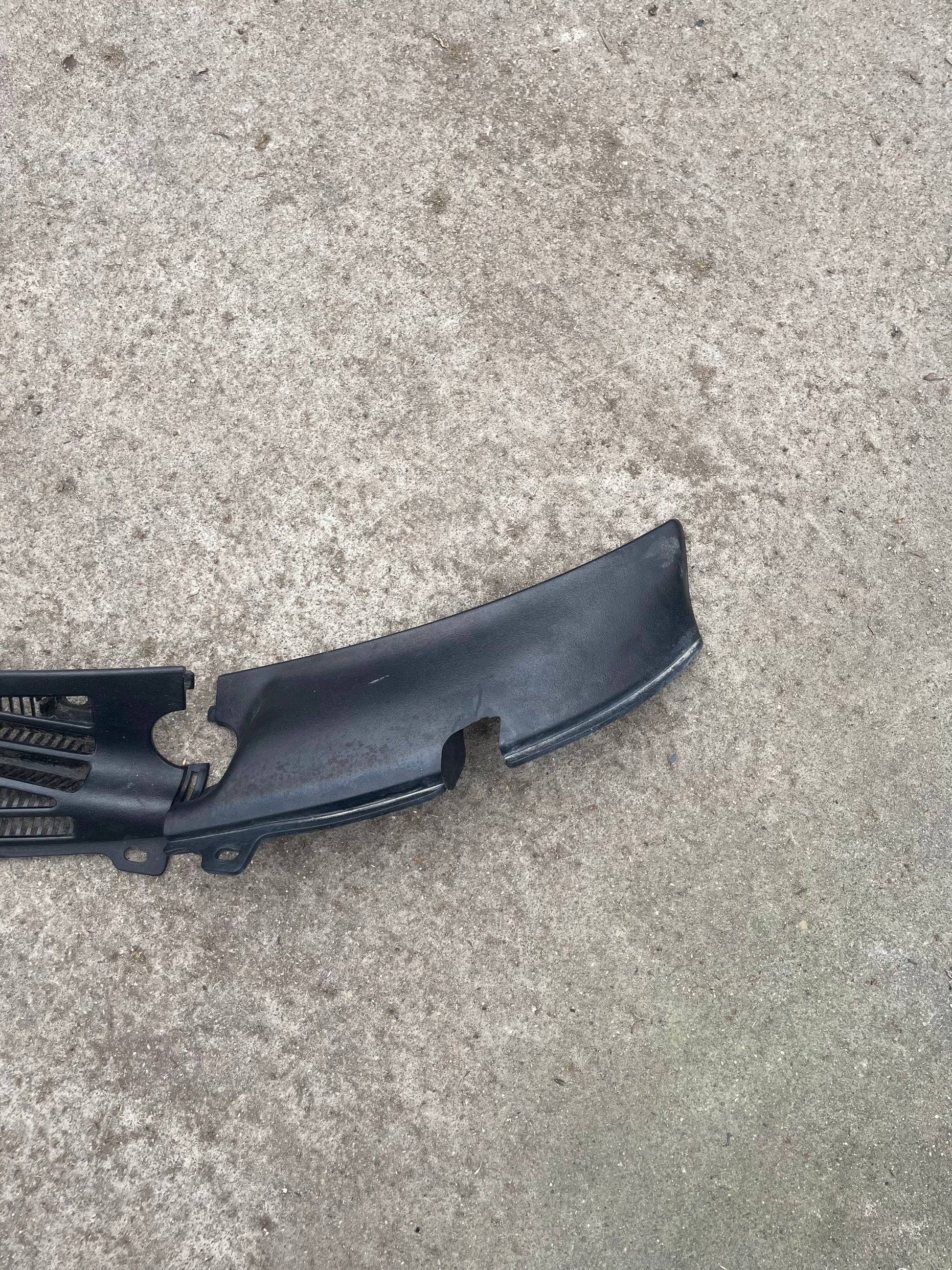 A black, textured OEM Wiper Cowl Cover Set by General Motors for 1994-2005 Chevrolet S10, Blazer, and more is shown on a rough gray concrete surface. It features mounting holes and grooves and is made of plastic.