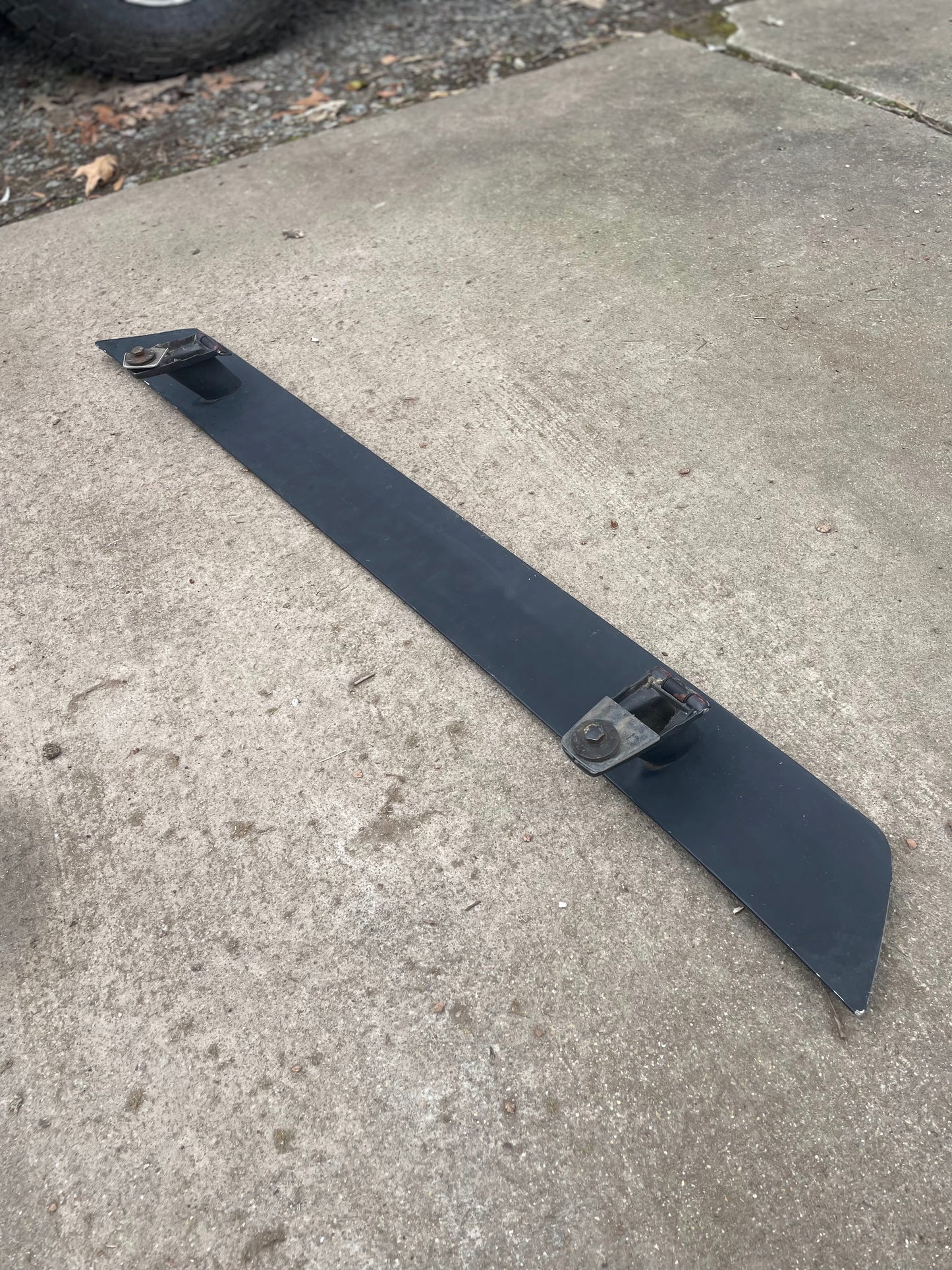 A General Motors OEM Rear Hatch Hinges with Spoiler Wing for 1983-1994 Chevrolet S10 Blazer and more is seen lying on a concrete surface outdoors.