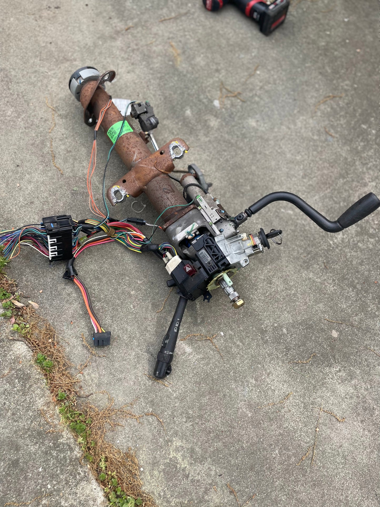 A General Motors OEM Steering Column w/KEY for 2000-2002 GM Full Size Trucks, with wiring, connectors, ignition parts, and an automatic transmission lever, is shown on a concrete surface with visible exposed cables.