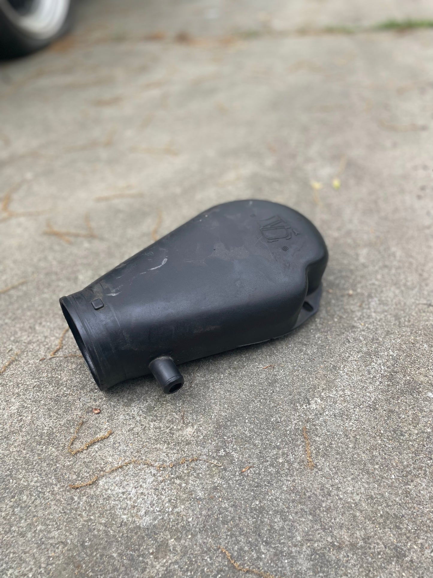 A black plastic General Motors OEM Cold Air Intake Hat 25147235 for a 4.3L 1996-2005 Chevrolet S10 and Blazer lies on concrete. Its rounded, tapered shape with a short nozzle suits cold air intake setups.