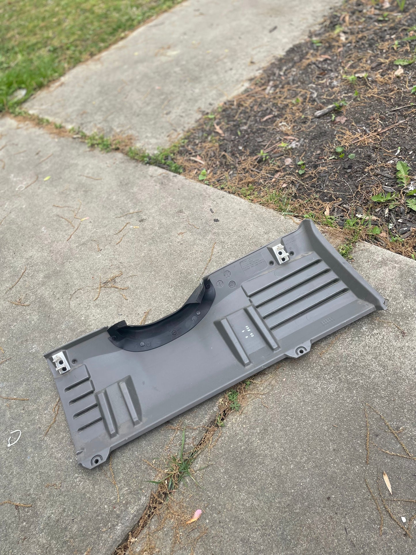 A General Motors OEM Center Console in Light Gray 92I for 2003-2007 Chevy Silverado, Tahoe, Suburban, and more sits on a concrete sidewalk near grass and soil, surrounded by twigs and debris.
