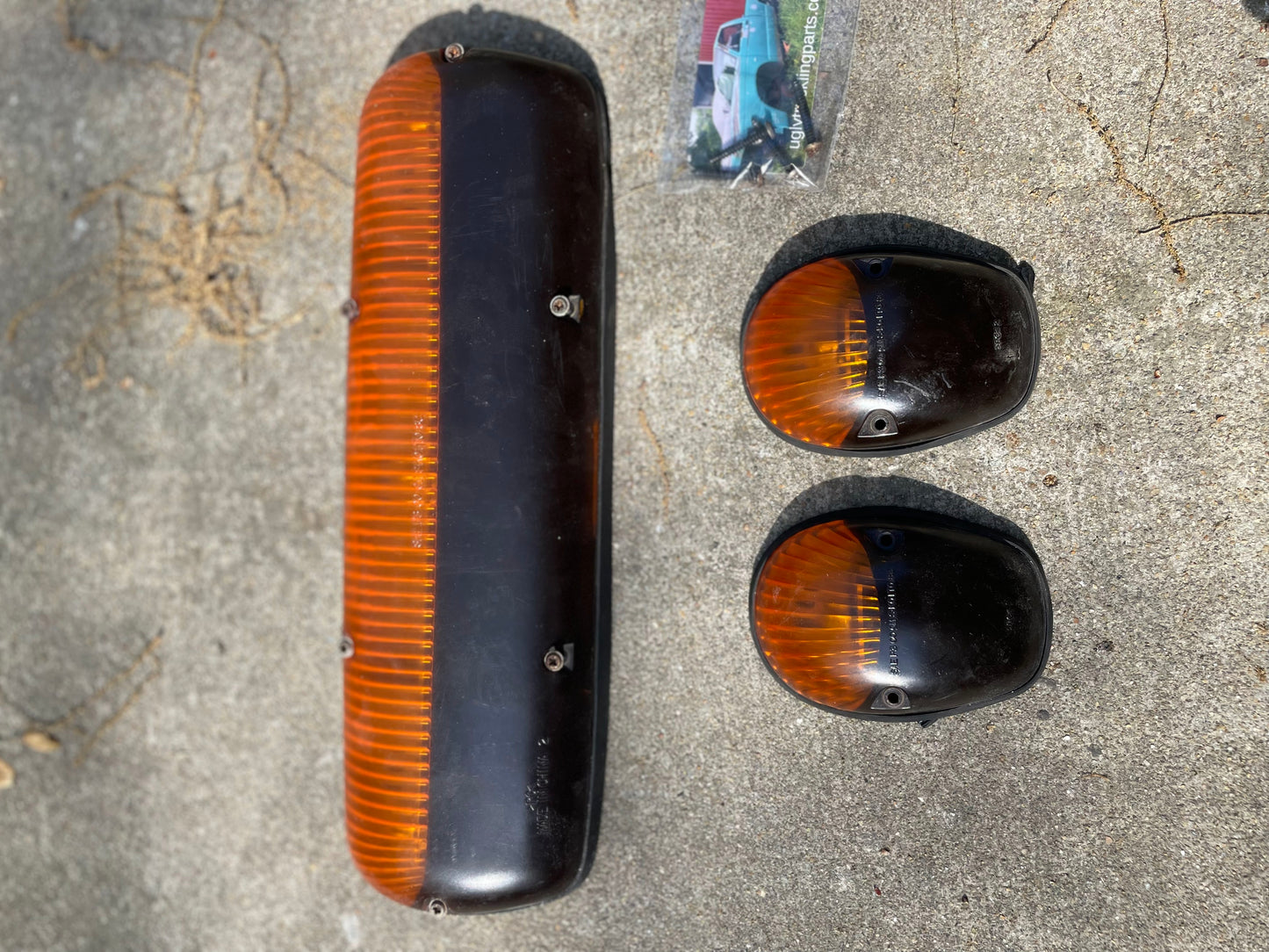 Three amber General Motors OEM Roof Light Lamp Cab Lenses—one large rectangular and two smaller rounded—are shown on concrete with a small plastic bag nearby, designed for 2000–2007 Chevrolet Silverado, Suburban, and more.