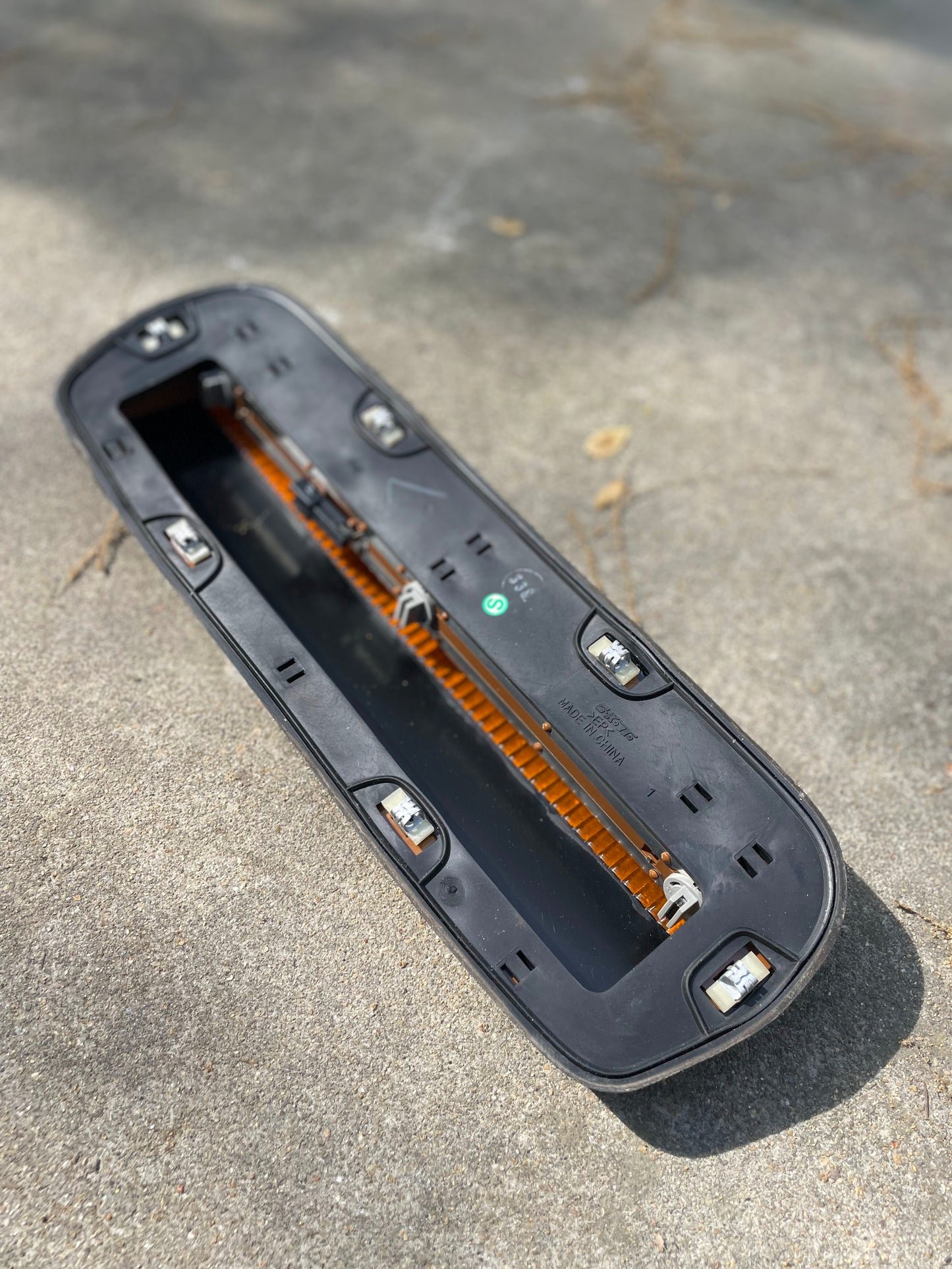 A close-up of a General Motors OEM Set Left Right Center Clearance Roof Light Lamp Cab Lens for 2000-2007 Chevrolet Silverado, Suburban, and more, with clips and visible circuit board, lying face down on outdoor concrete in sunlight.
