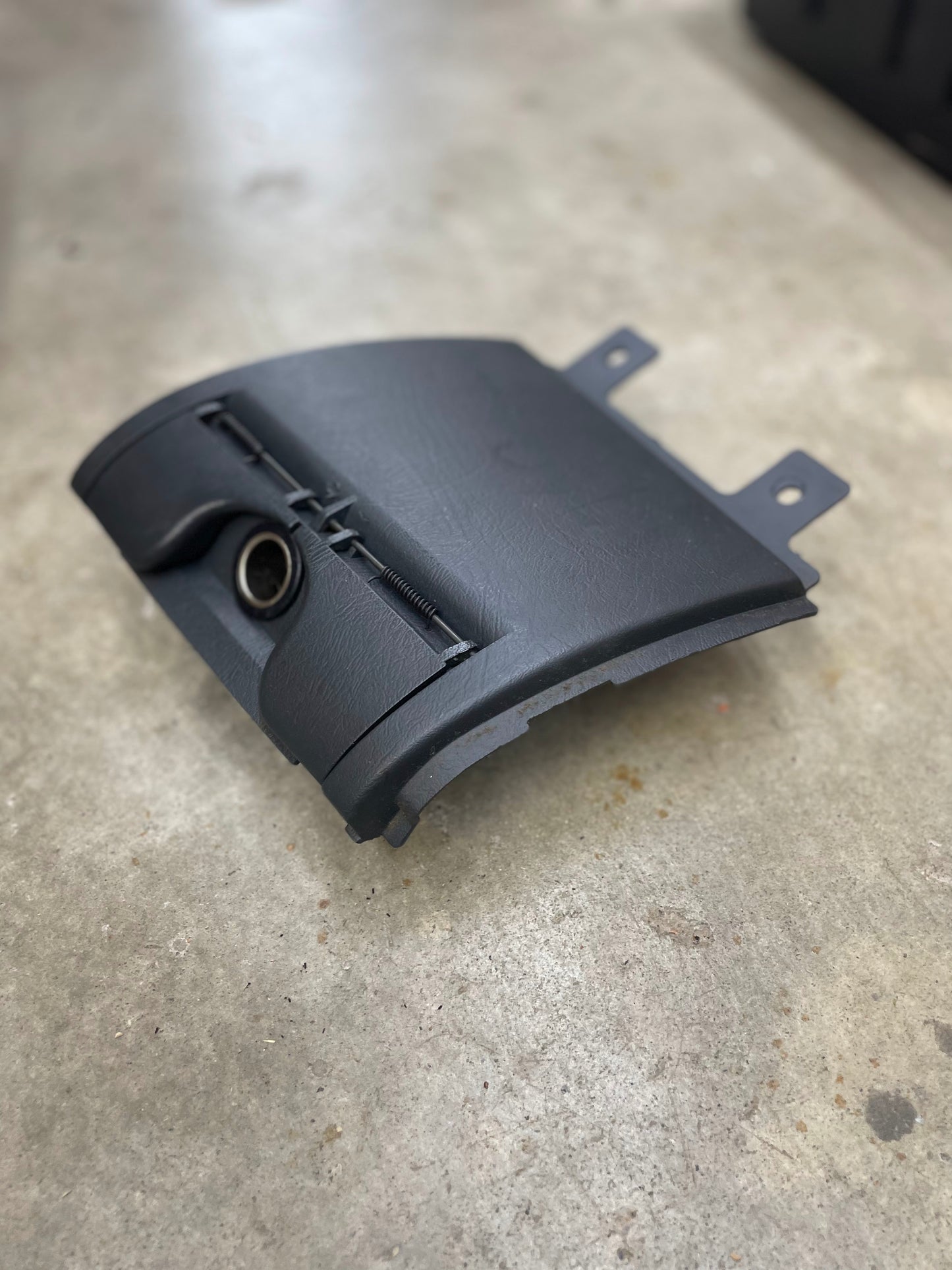 A General Motors OEM 3 Port 12V Aux Panel Ash Tray Delete in dark gray, made for 1998-2000 GMC Envoy, rests on a concrete floor.