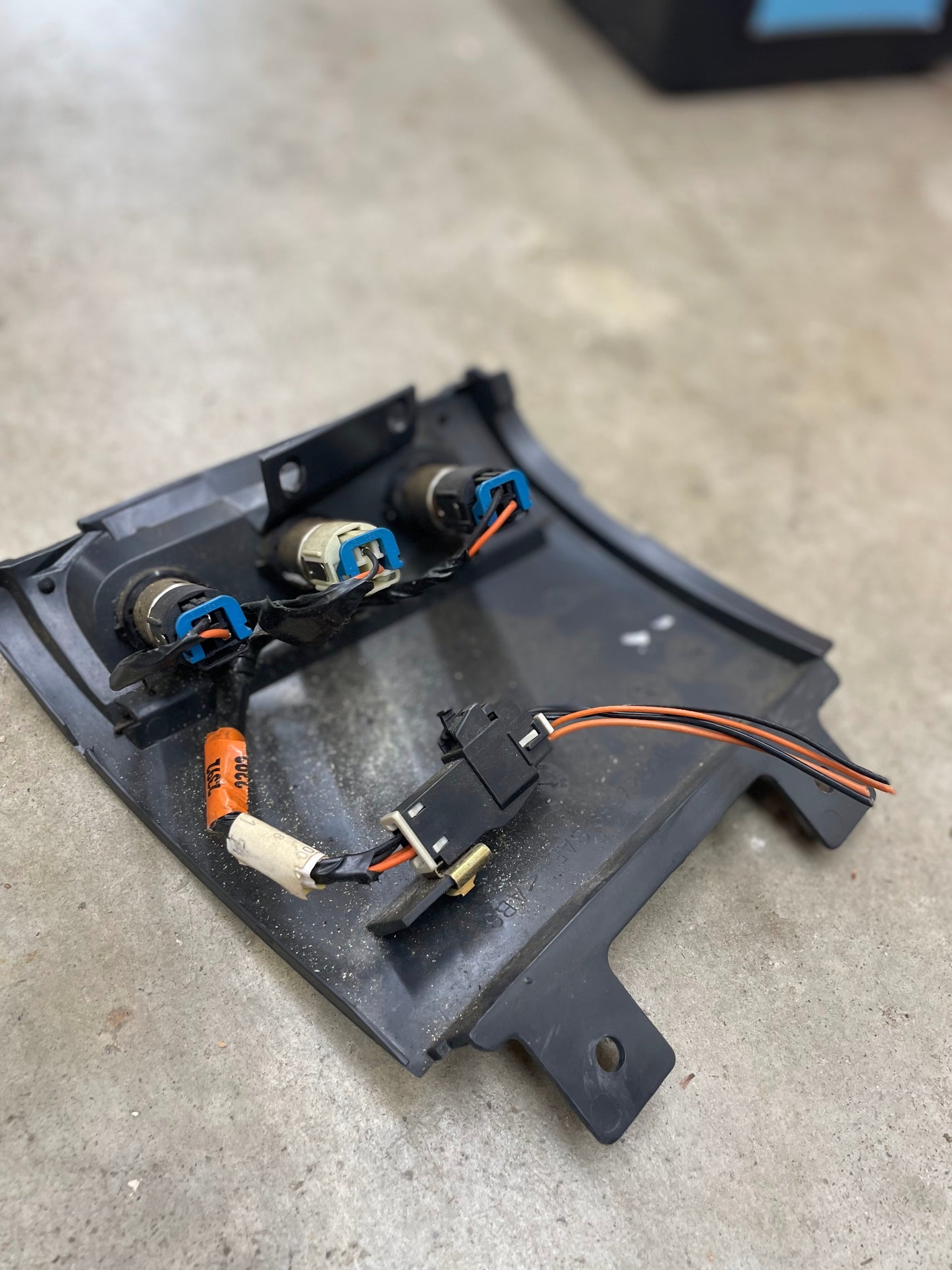 A General Motors OEM 3 Port 12V Aux Panel Ash Tray Delete in dark gray (1998-2000 GMC Envoy) with wiring and bulb sockets is shown on a concrete floor, ideal for 12V outlet panel or interior trim upgrades.