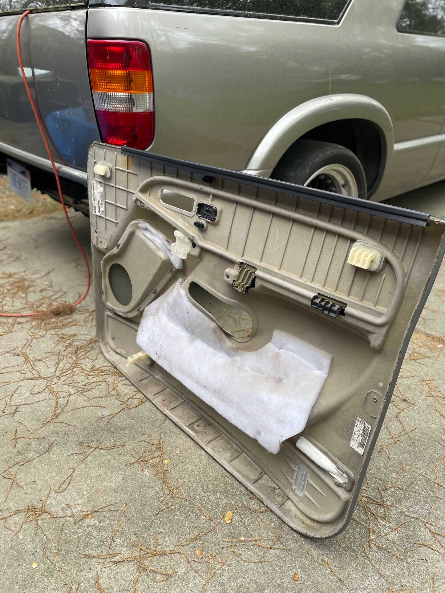 A pair of OEM General Motors front leather door trim panels in light gray, for 2003-2006 Chevy Silverado/GMC Sierra, are shown detached near a gray SUV with Pewter interior, possibly on a concrete driveway.