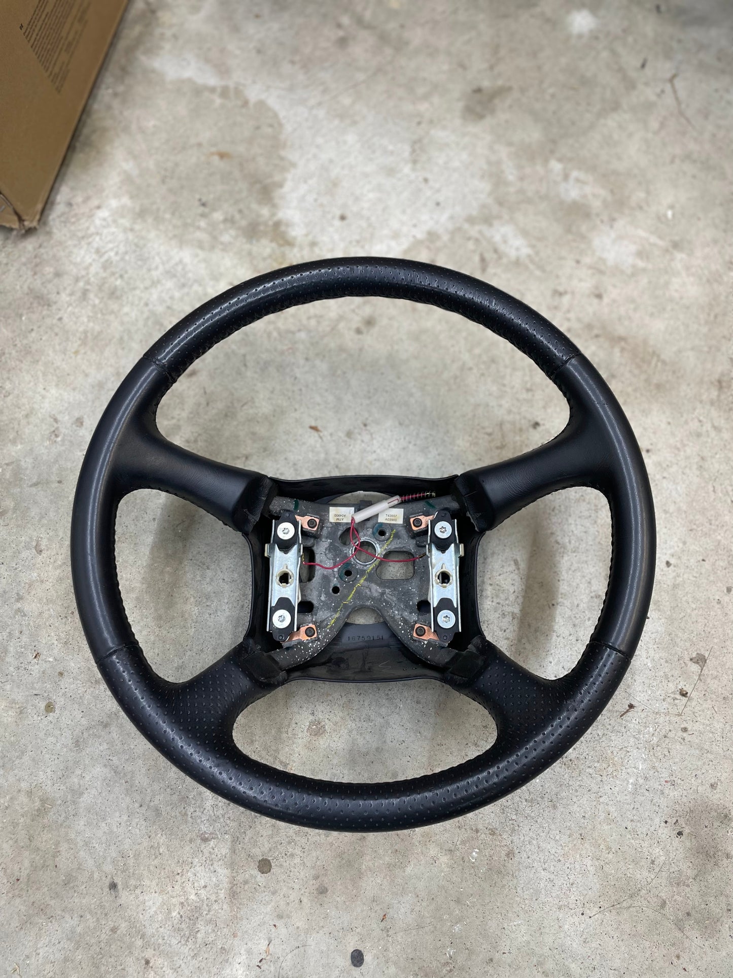 A General Motors OEM Perforated Leather Steering Wheel for 1999-2005 Chevy Silverado, S10, and more is shown without its center cover, exposing the mounting hardware and internal mechanism.