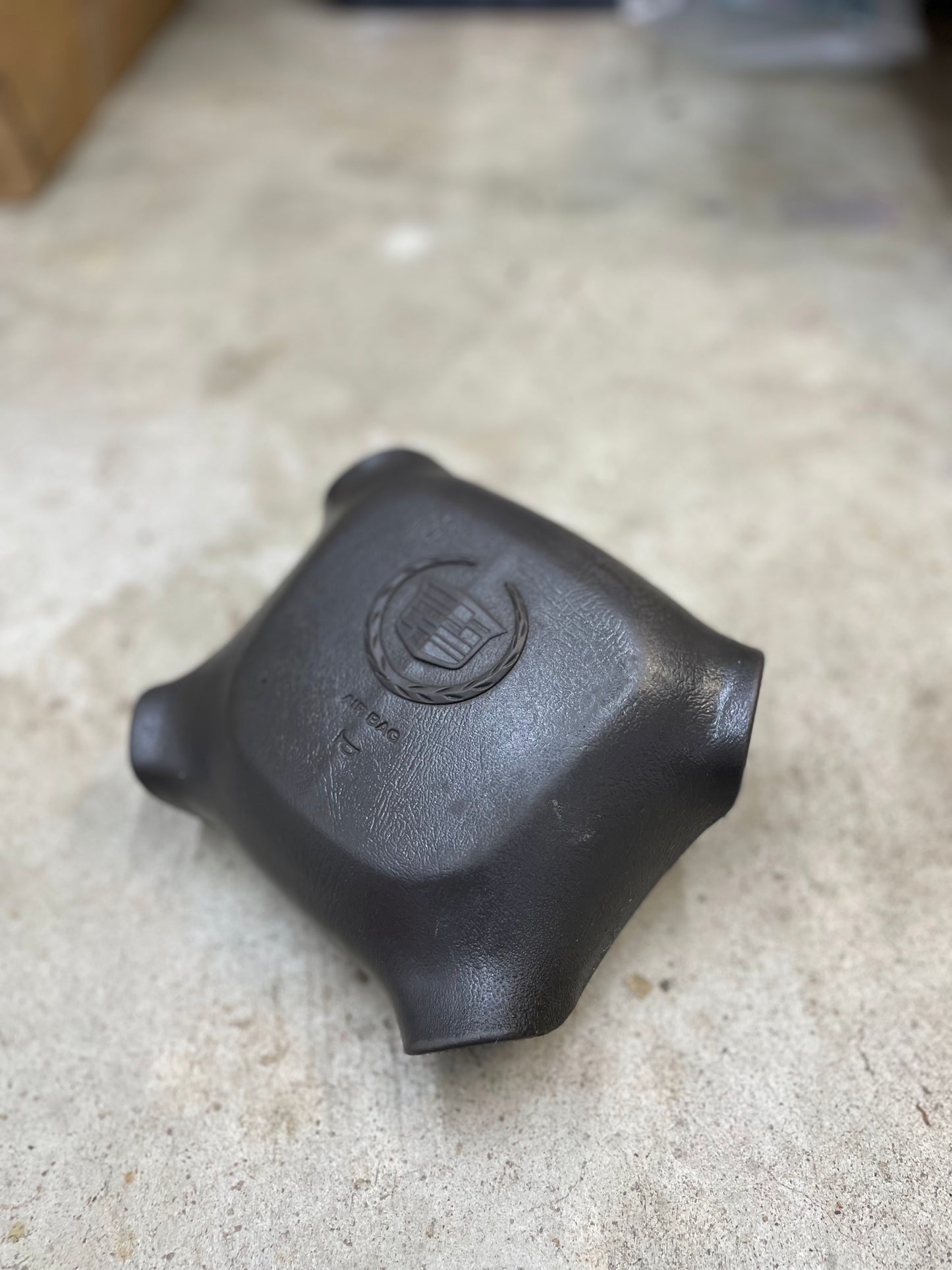 A General Motors KIT Leather w/Wood Steering Wheel with radio controls for 1995–2005 GM Trucks, featuring the original design, is shown resting on a concrete surface with a blurred background.