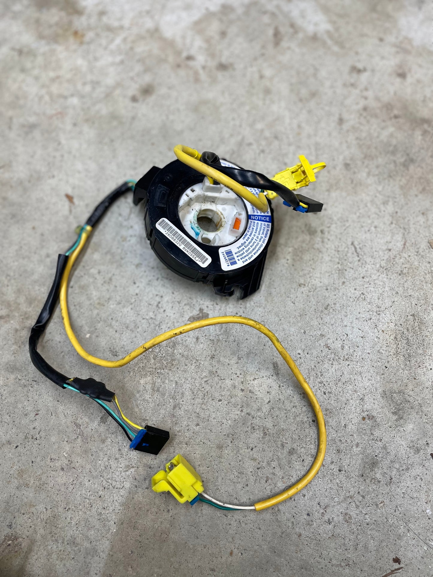 A General Motors KIT Leather w/Wood Steering Wheel & Radio Controls from Escalade (fits 1995-2005 GM Trucks) with airbag clock spring, yellow/black wiring, connectors, labels, and a circular central component rests on a concrete surface.