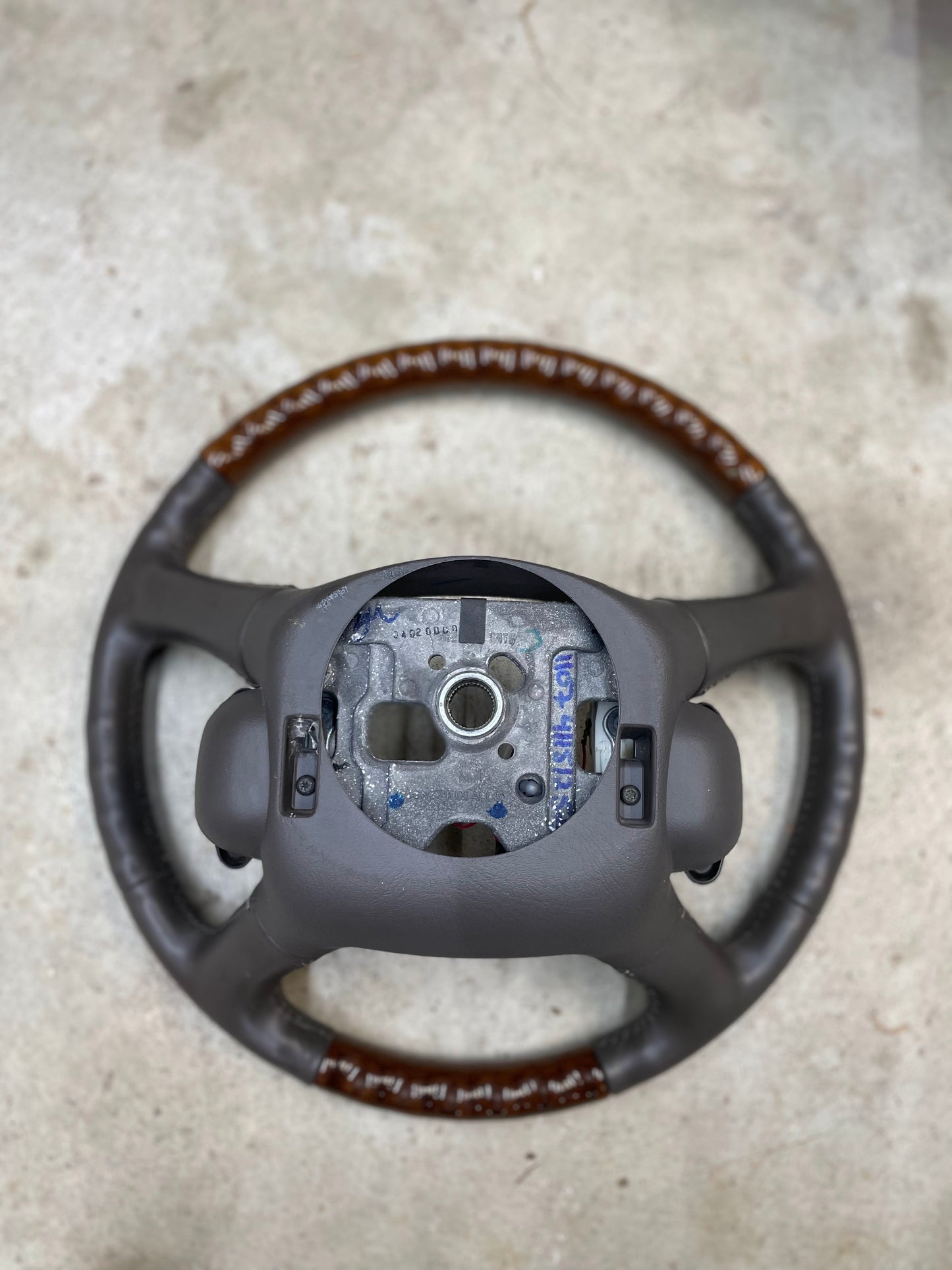 A General Motors KIT Leather w/Wood Steering Wheel & Radio Controls from Escalade, fitting 1995-2005 GM Trucks, rests on a light-colored concrete surface.
