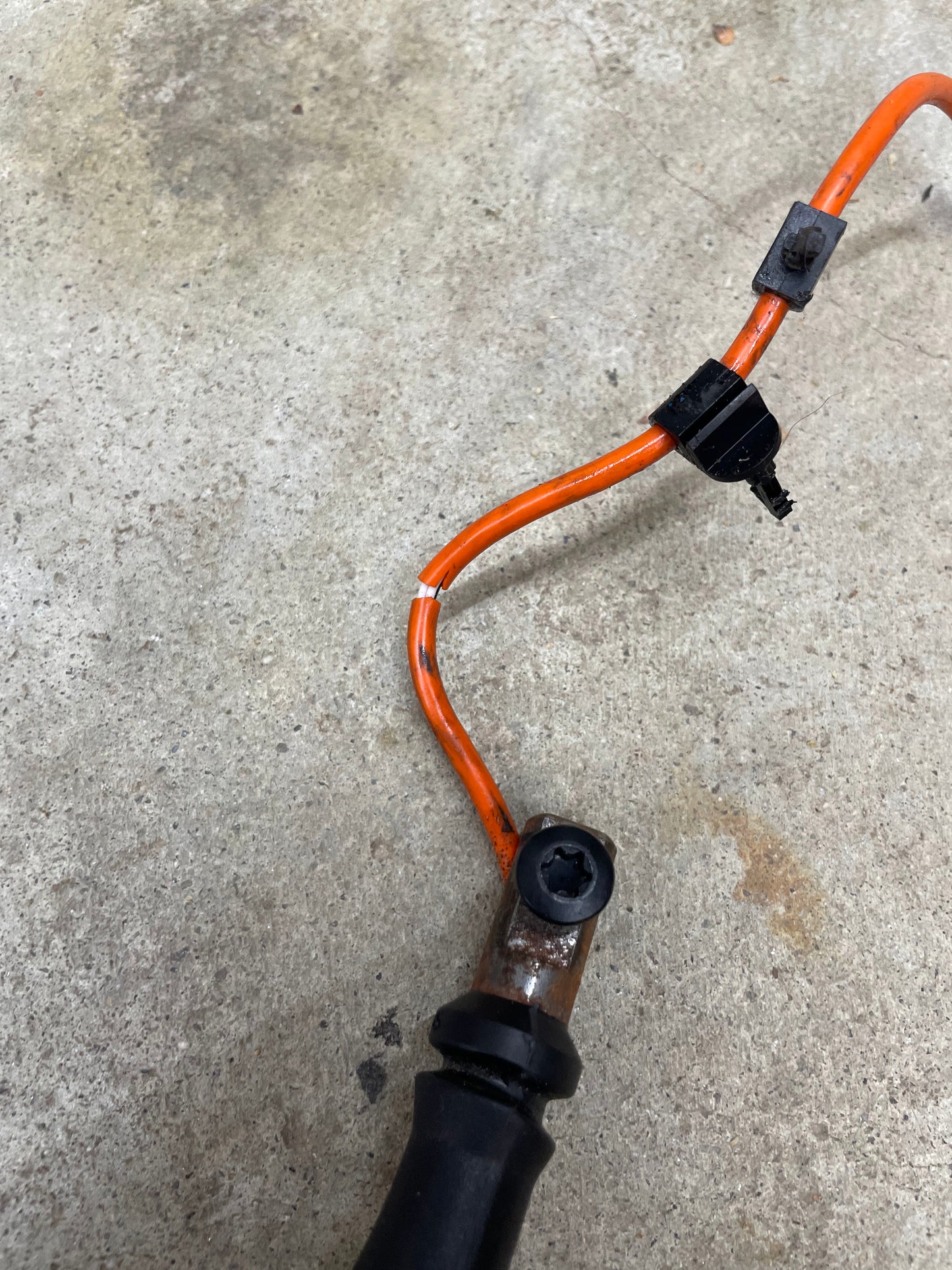 An OEM Column Shift Lever with Tow/Haul & Tapshift for 2006-2007 GM Duramax LBZ by General Motors lies on rough, light concrete, showing a worn wire with some exposed metal and discoloration near the connector.