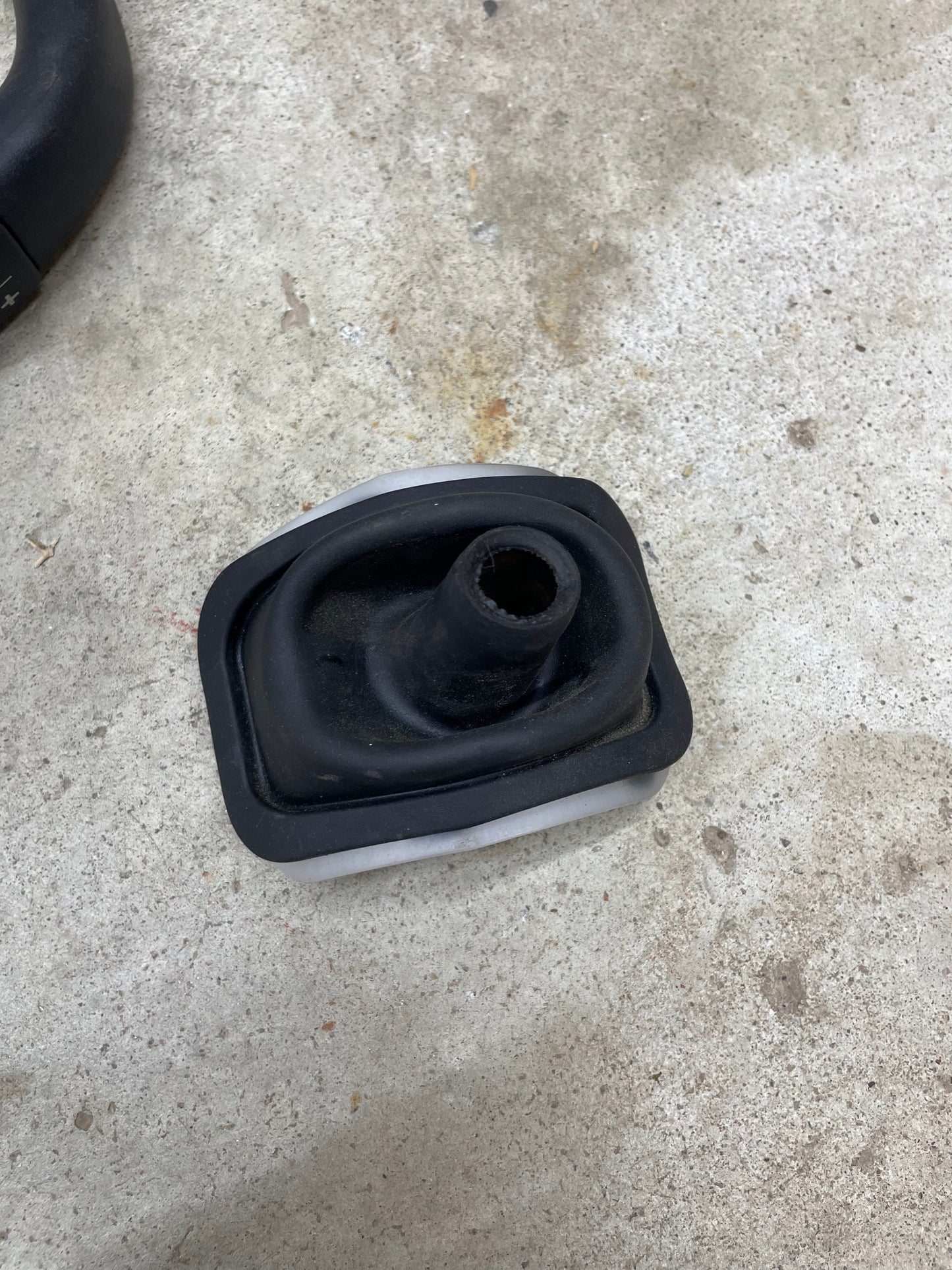 A black rubber boot with a central hole rests on rough, light-colored concrete. It appears used and slightly dusty, possibly from a General Motors OEM Column Shift Lever with Tow/Haul & Tapshift for 2006-2007 Duramax LBZ.