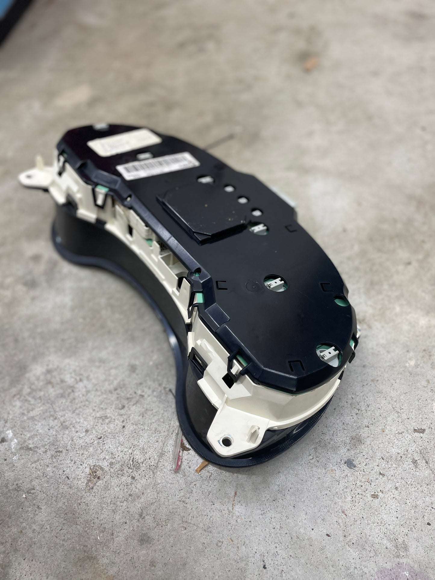 A General Motors OEM Tested Instrument Cluster with Tachometer for 2001-2005 Chevy S10 or Blazer with Console Shifter rests on a concrete floor, shown from the rear and side angle.