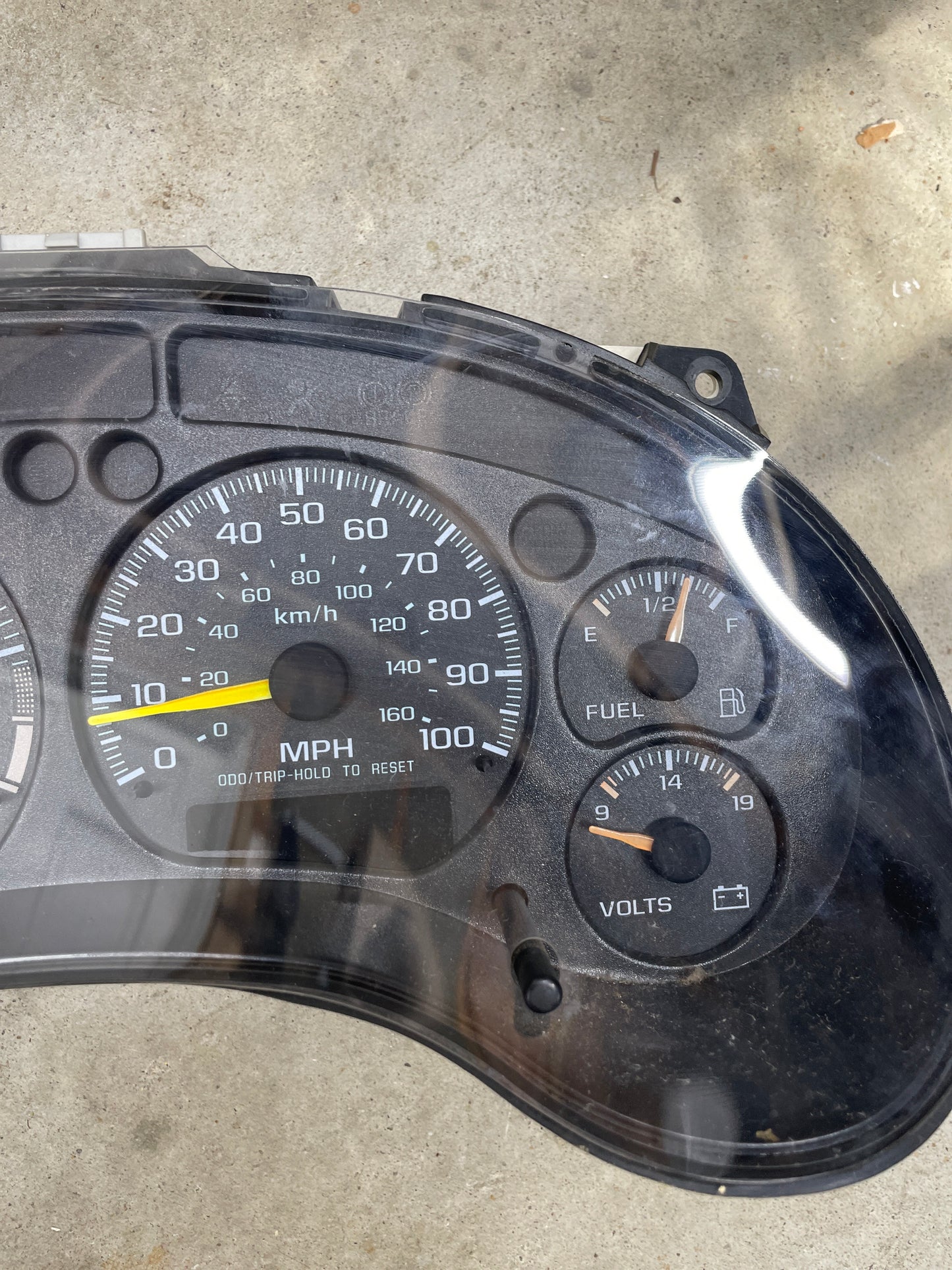 A close-up of the General Motors OEM Tested Instrument Cluster with Tachometer for 2001-2005 Chevy S10 or Blazer (console shifter), showing speedometer, fuel, temp, and voltmeter gauges on a concrete surface with reflections on the clear cover.