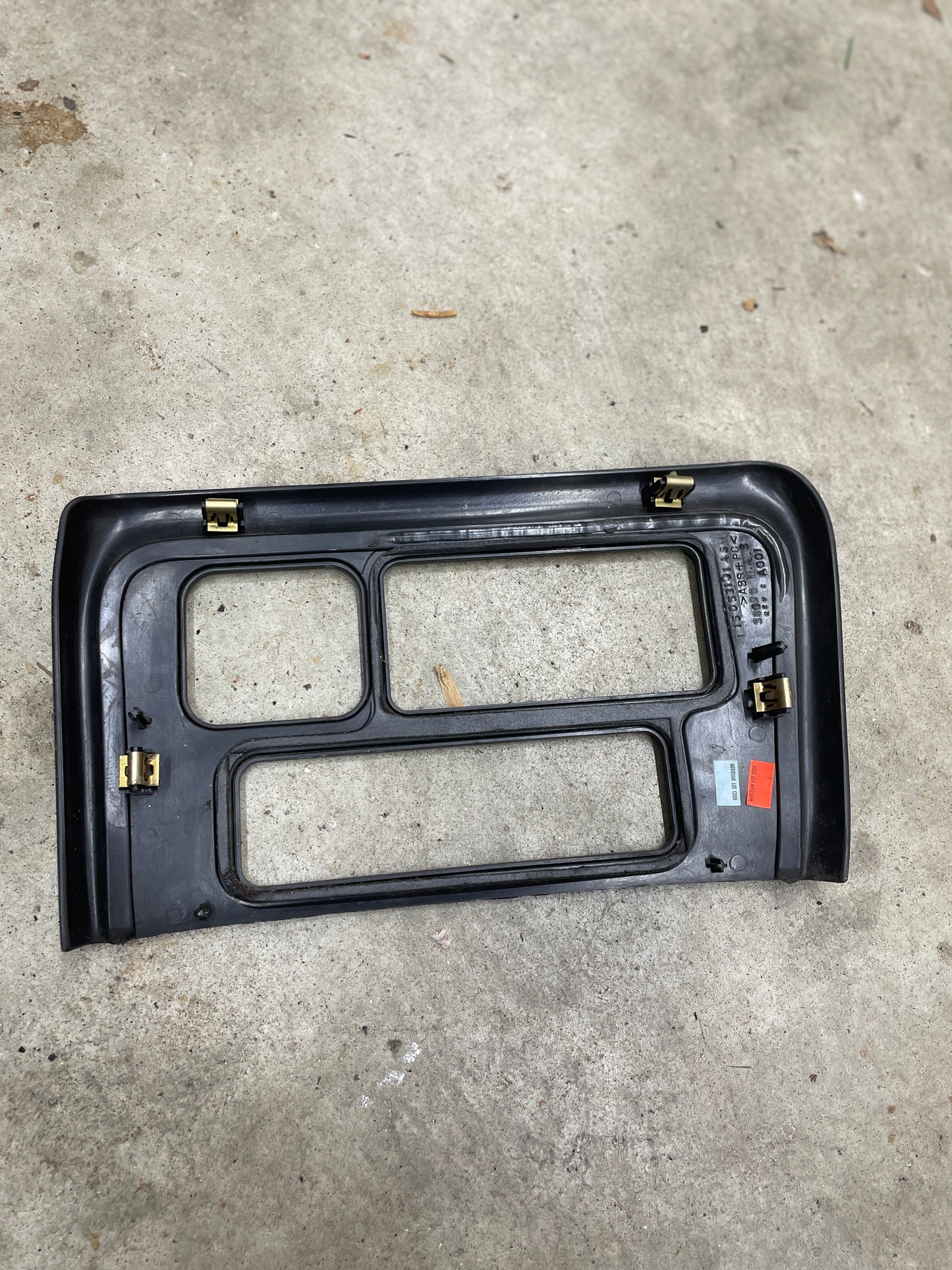 A General Motors OEM Center Console Front Bin Dark Woodgrain Trim for 2001-2002 GMC Sierra C3 and Yukon Denali with two large cutouts and metal clips is placed on a concrete floor, showing labels and stickers in the lower right corner.