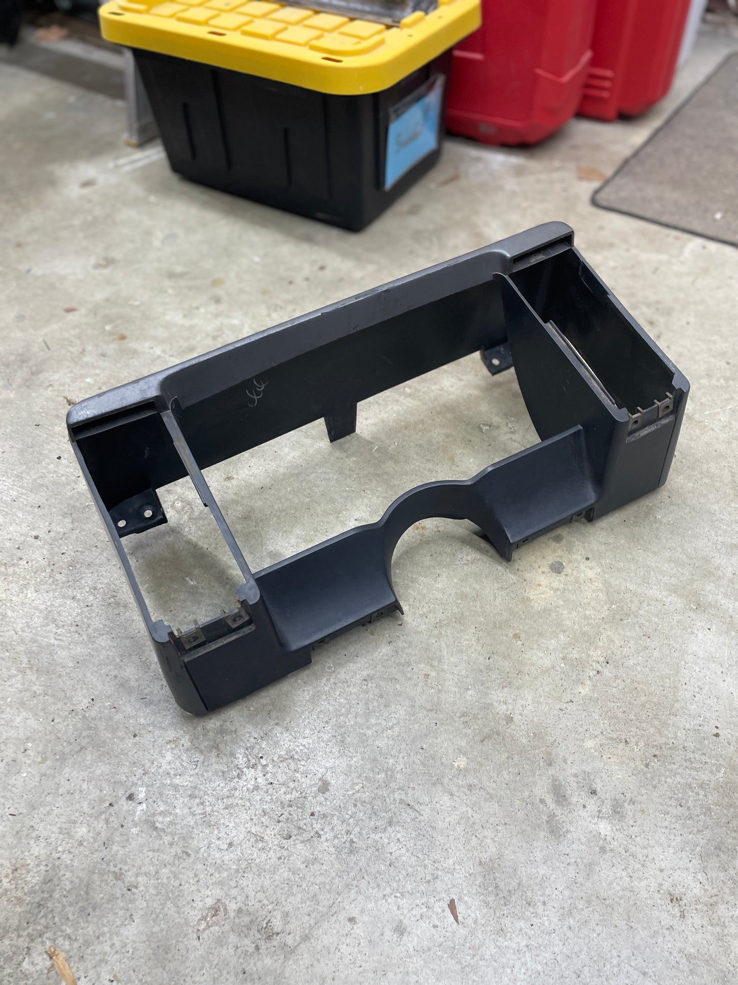 An OEM gray instrument cluster dash bezel by General Motors for 1986–1993 Chevy S10, Blazer, GMC S15, and more rests on a concrete garage floor with storage bins and containers in the background.