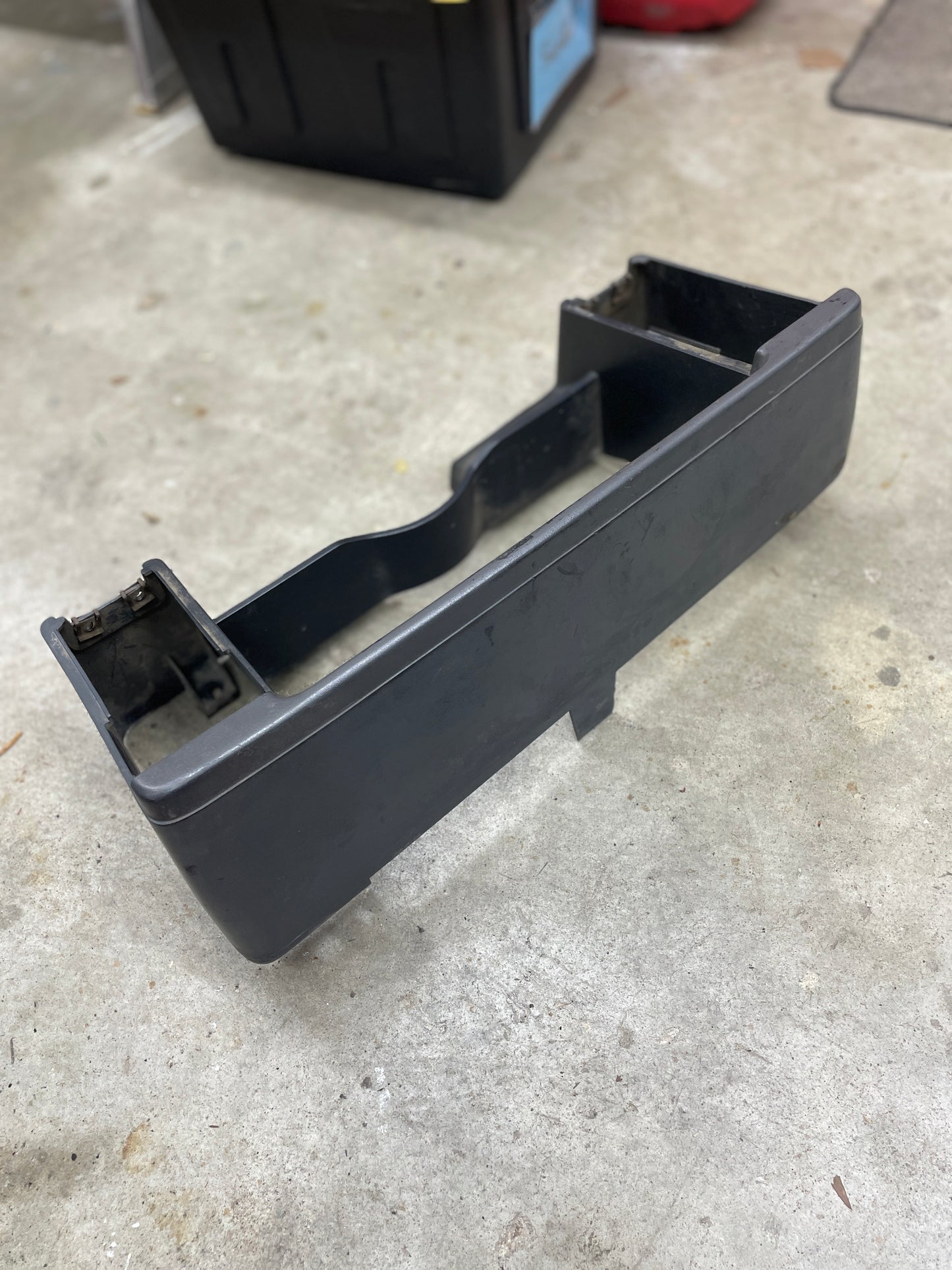 A gray OEM Instrument Cluster Dash Bezel by General Motors for 1986-1993 Chevy S10 Blazer and GMC S15 lies on a concrete garage floor, surrounded by storage bins and tools.