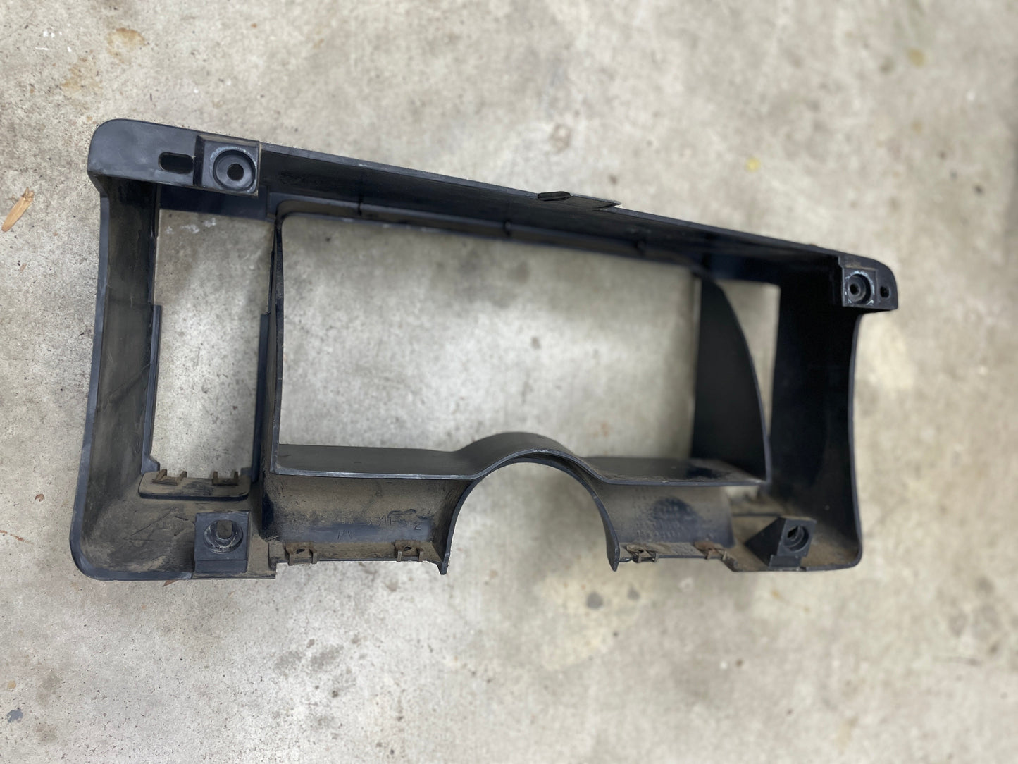 A gray General Motors OEM instrument cluster dash bezel for 1986-1993 Chevy S10 Blazer and GMC S15 is shown on concrete, displaying some dust and wear, with multiple mounting holes and rectangular cutouts.
