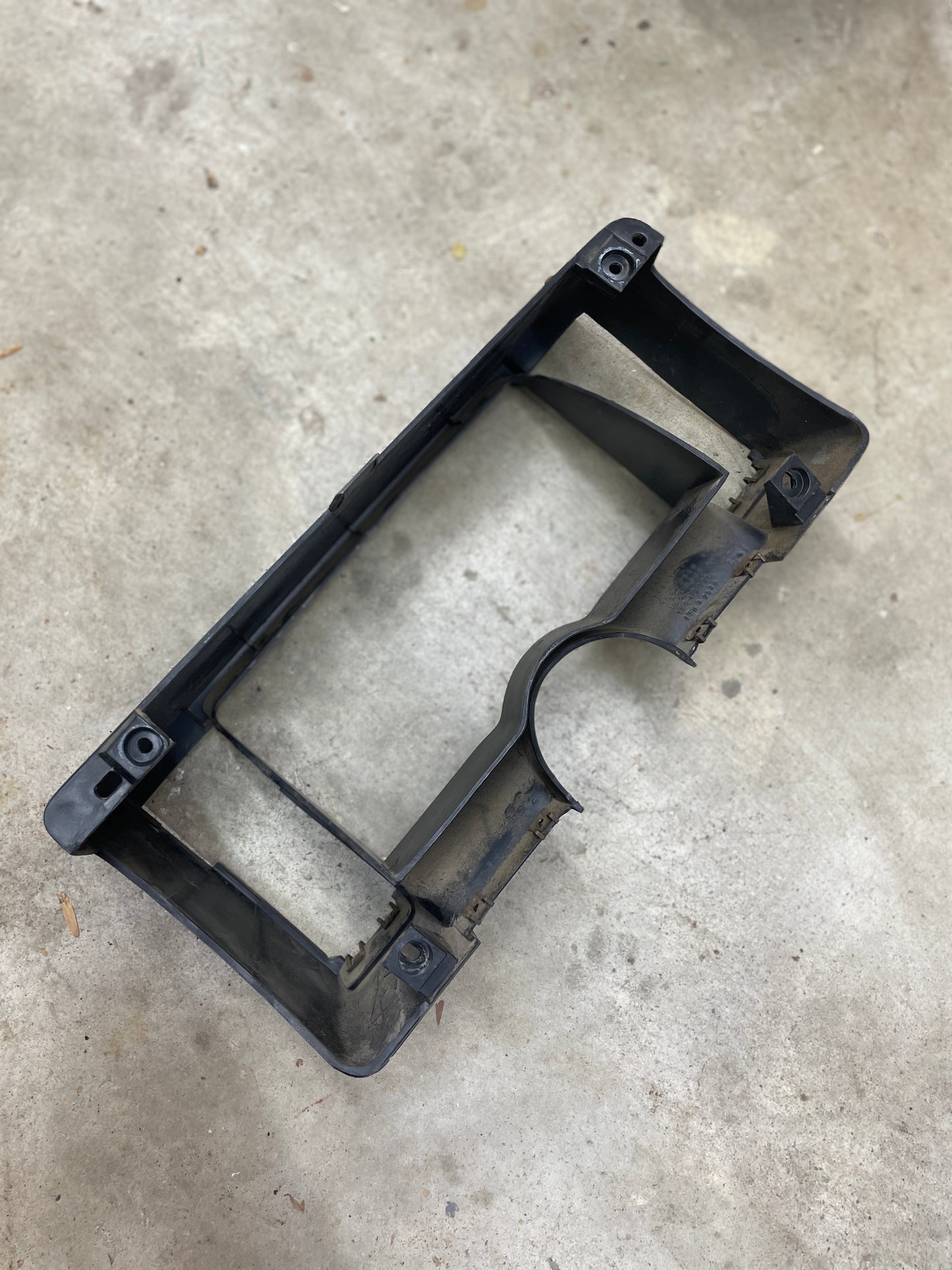 A used gray OEM Instrument Cluster Dash Bezel by General Motors for 1986-1993 Chevy S10 Blazer, GMC S15, and more is shown on a gray concrete floor with some dust and rust visible around the edges.