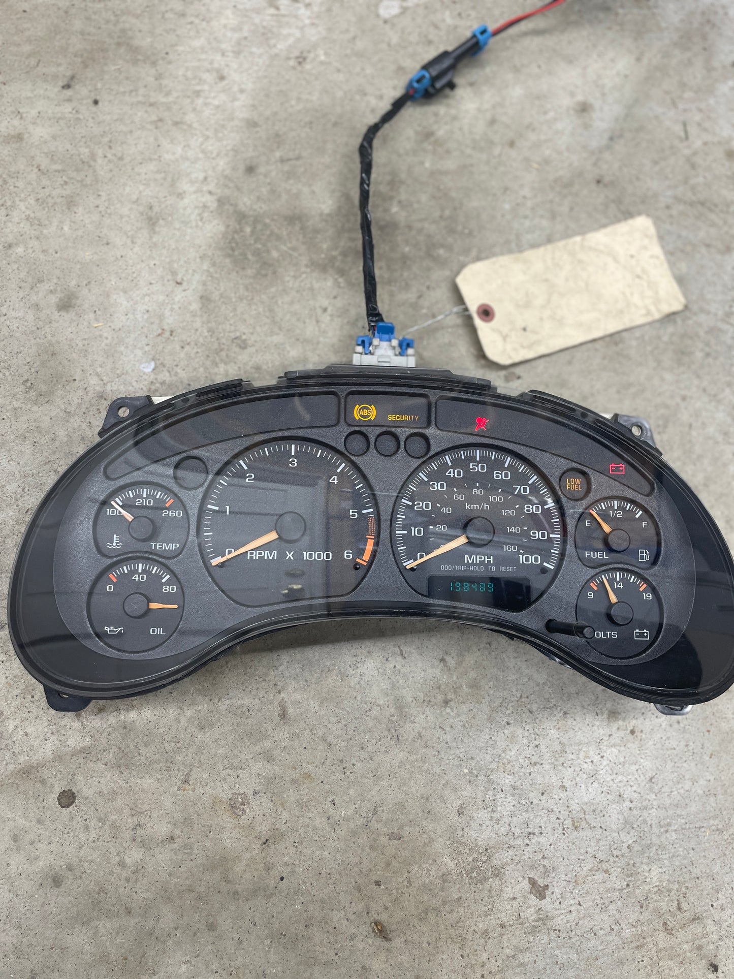 The General Motors OEM Tested Instrument Cluster with Tachometer for 2001–2005 Chevy S10 or Blazer with Console Shifter is shown detached on concrete, gauges and indicator lights visible, paper tag attached; fits manual transmission 4.3 V6 models.