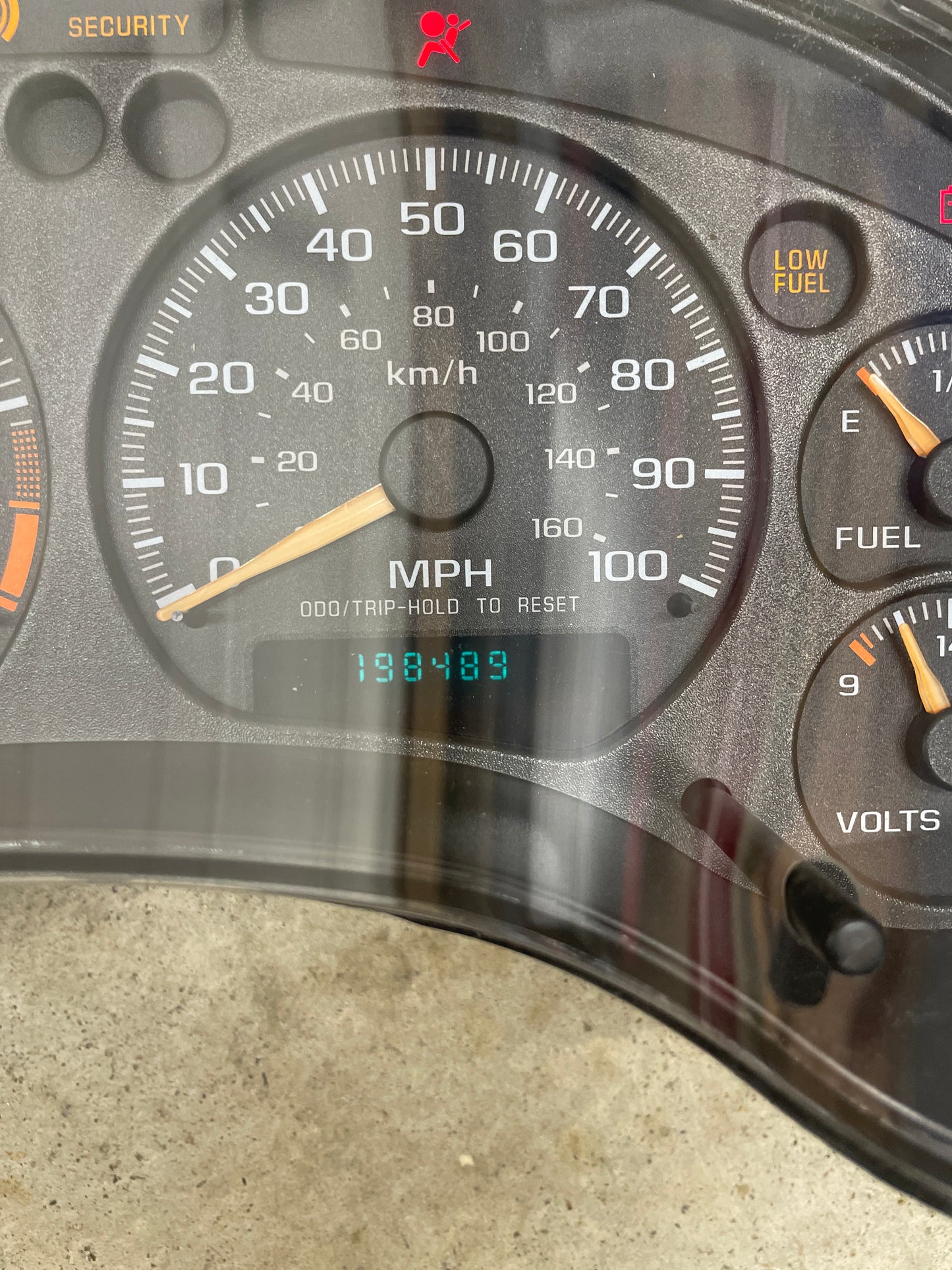 Close-up of a General Motors OEM Tested Instrument Cluster with Tachometer for 2001-2005 Chevy S10 or Blazer (console shifter), showing speedometer, odometer at 198489 miles, low fuel and security lights, plus fuel and voltage gauges.